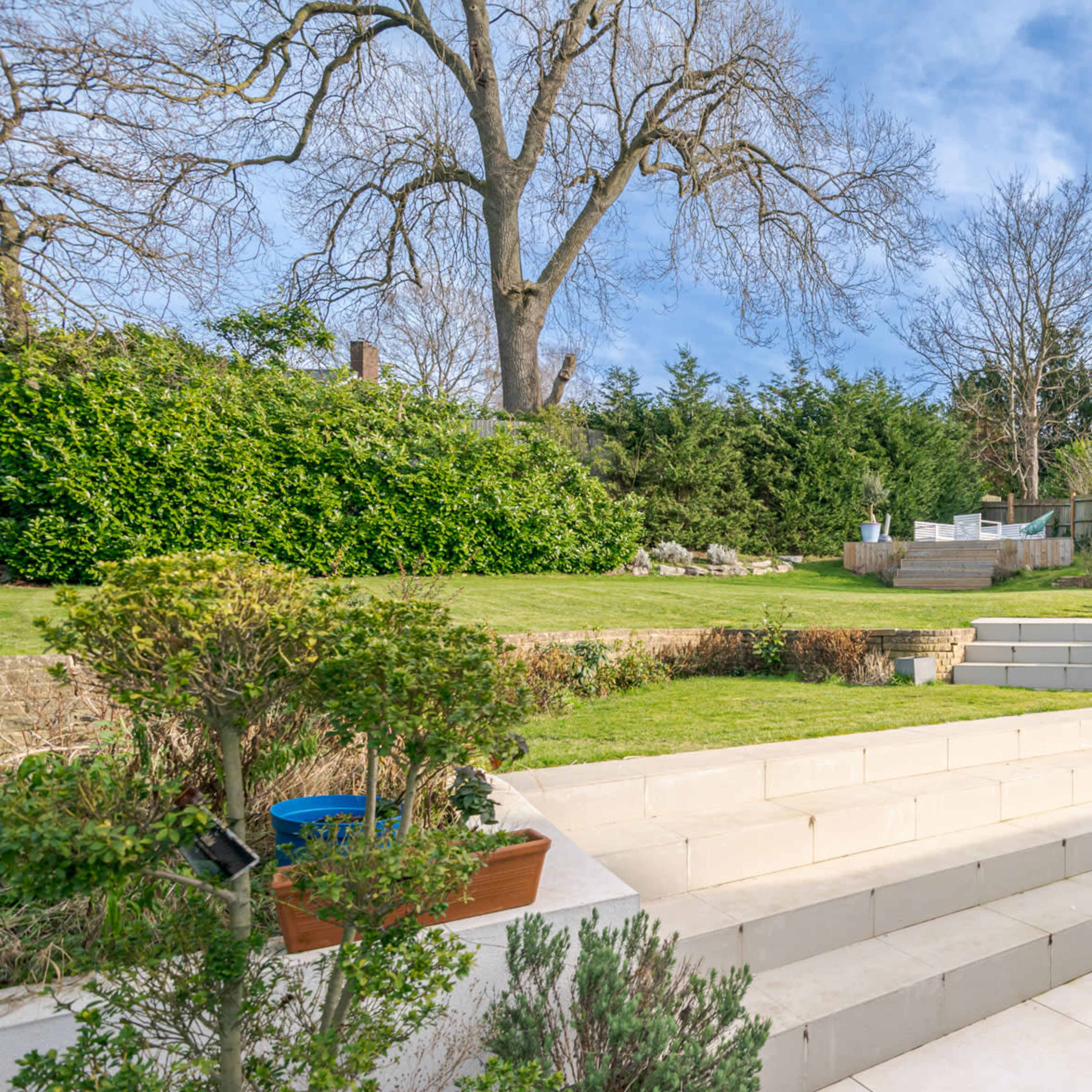 A landscaped backyard with tiered levels, stone steps, and various plants along the perimeter.