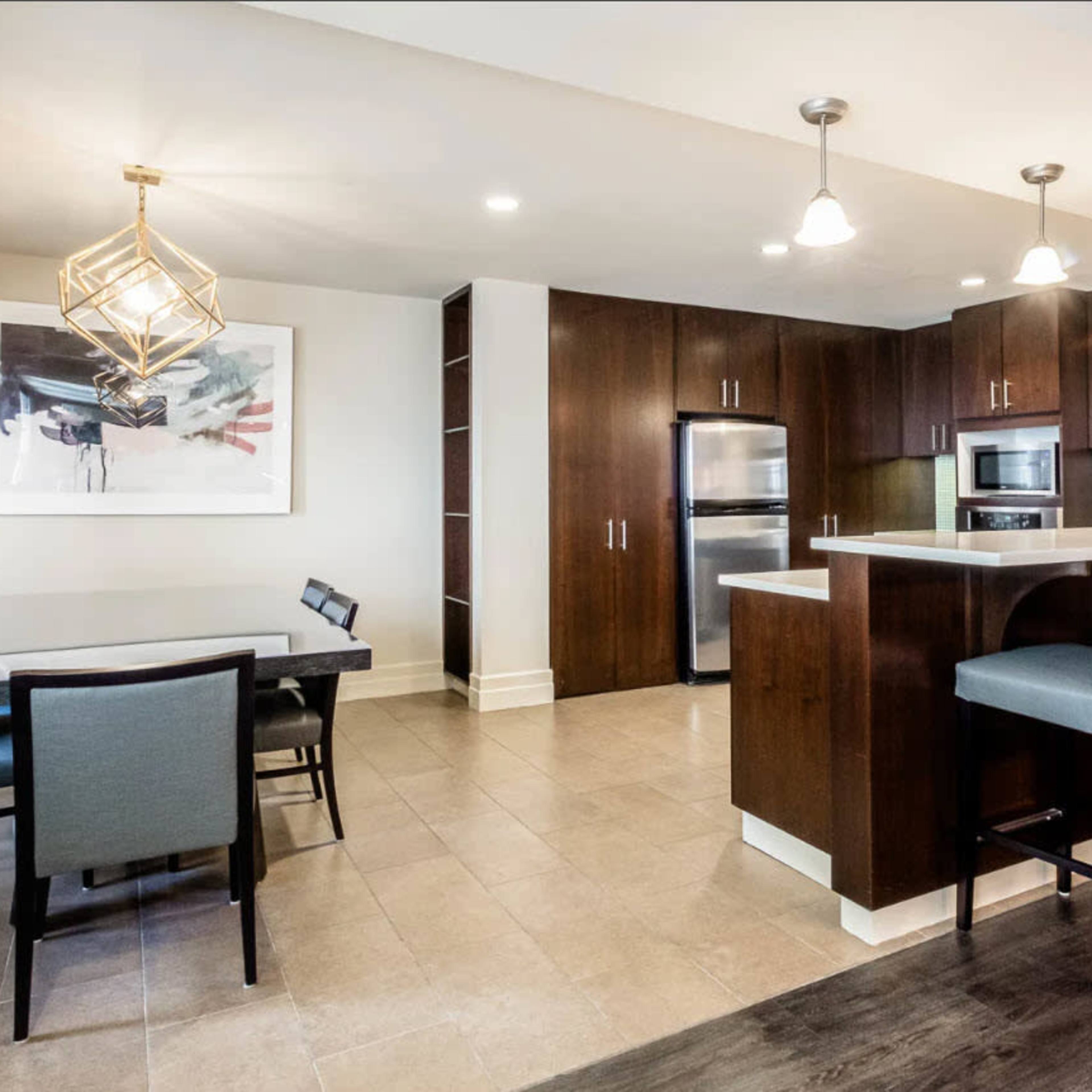 A modern kitchen and dining area featuring dark wood cabinetry, stainless steel appliances, a table with chairs, and bar seating at a kitchen counter.