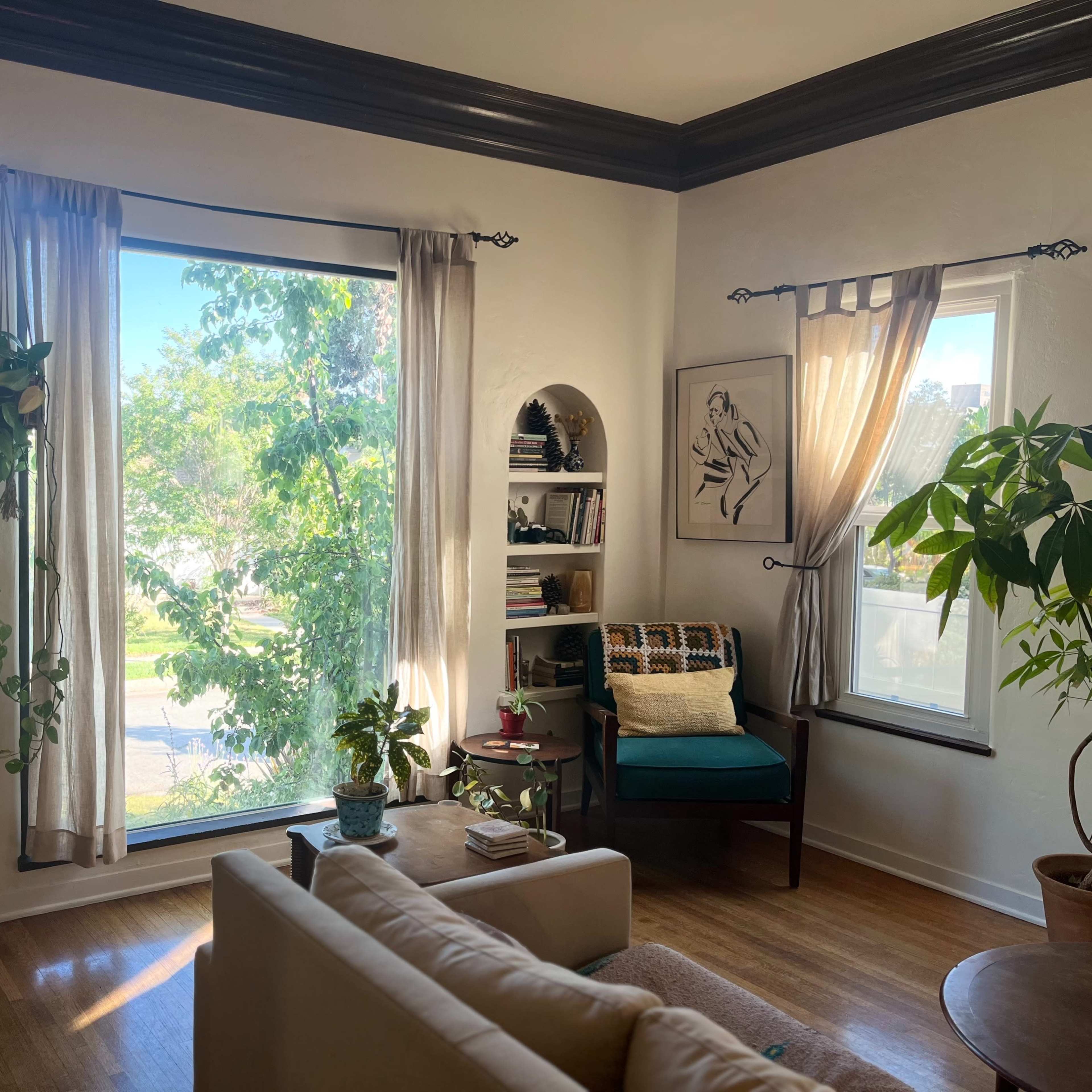 A bright living room with large windows, bookshelves on the walls, and a green armchair beside potted plants.