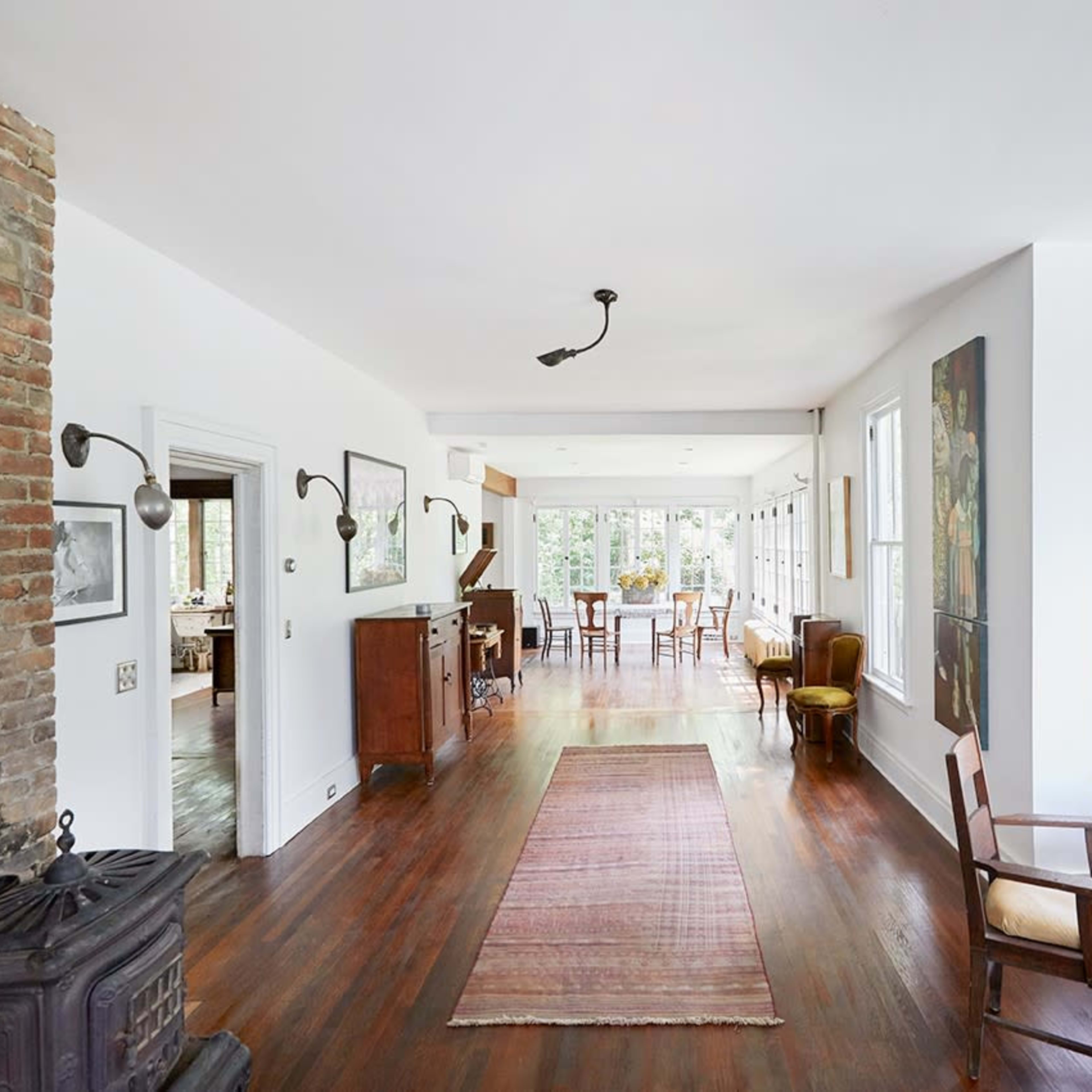 A spacious, bright interior of a home with wooden flooring, a brick wall, and large windows overlooking a garden area.