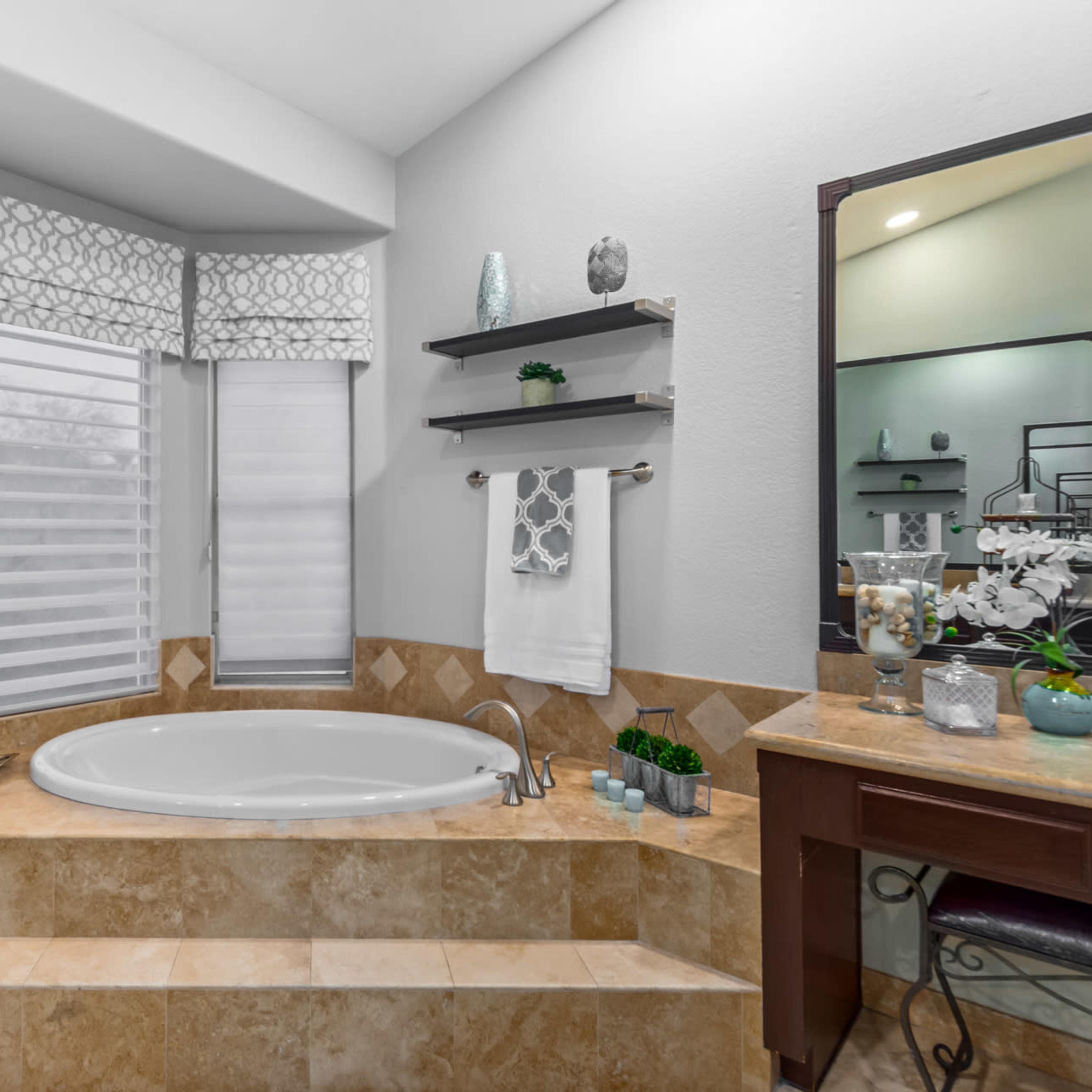A bathroom with a circular bathtub situated on a tiled ledge, accompanied by decorative elements and shelving above.