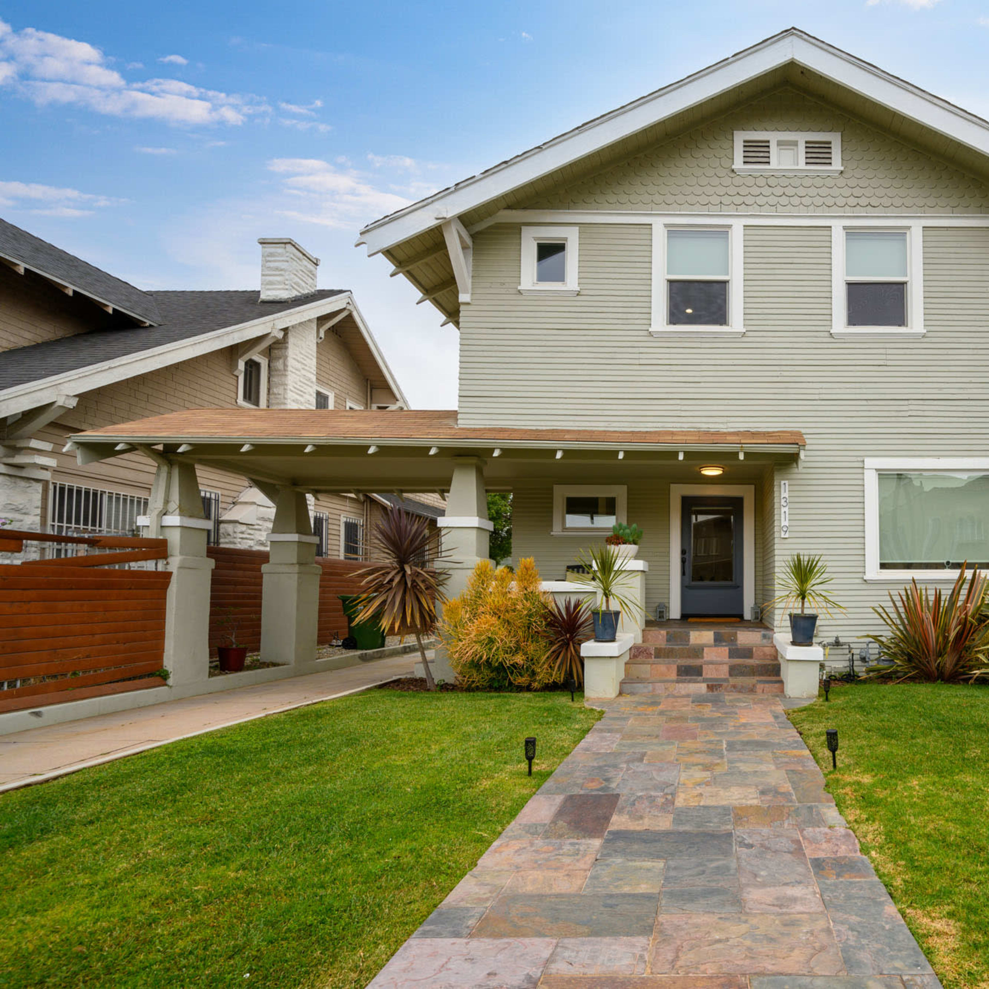 A two-story house with a light green exterior and a landscaped front yard featuring a stone pathway and various plants.