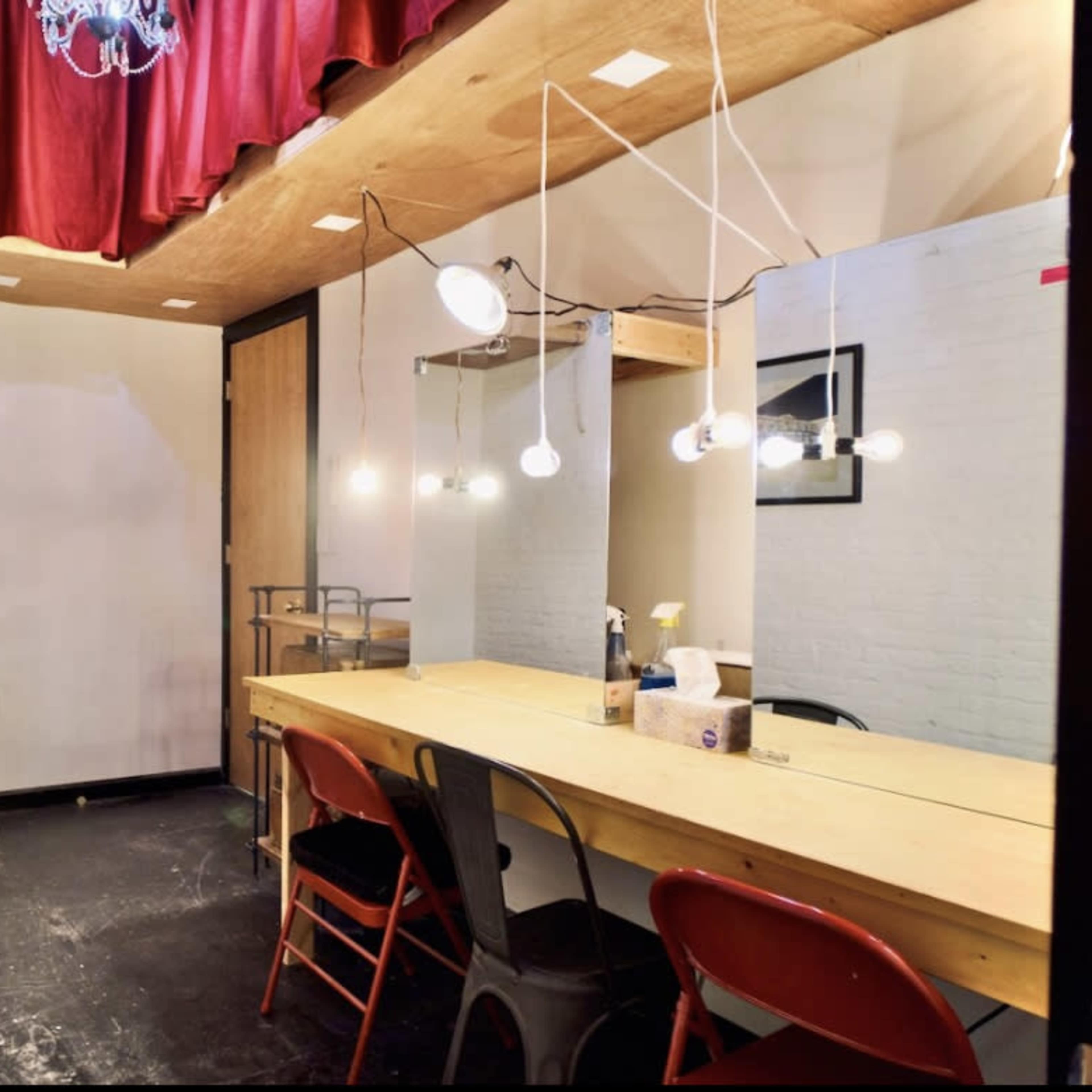 A small room featuring a long wooden table with several red chairs, a mirror on the wall, and soft lighting from hanging bulbs.