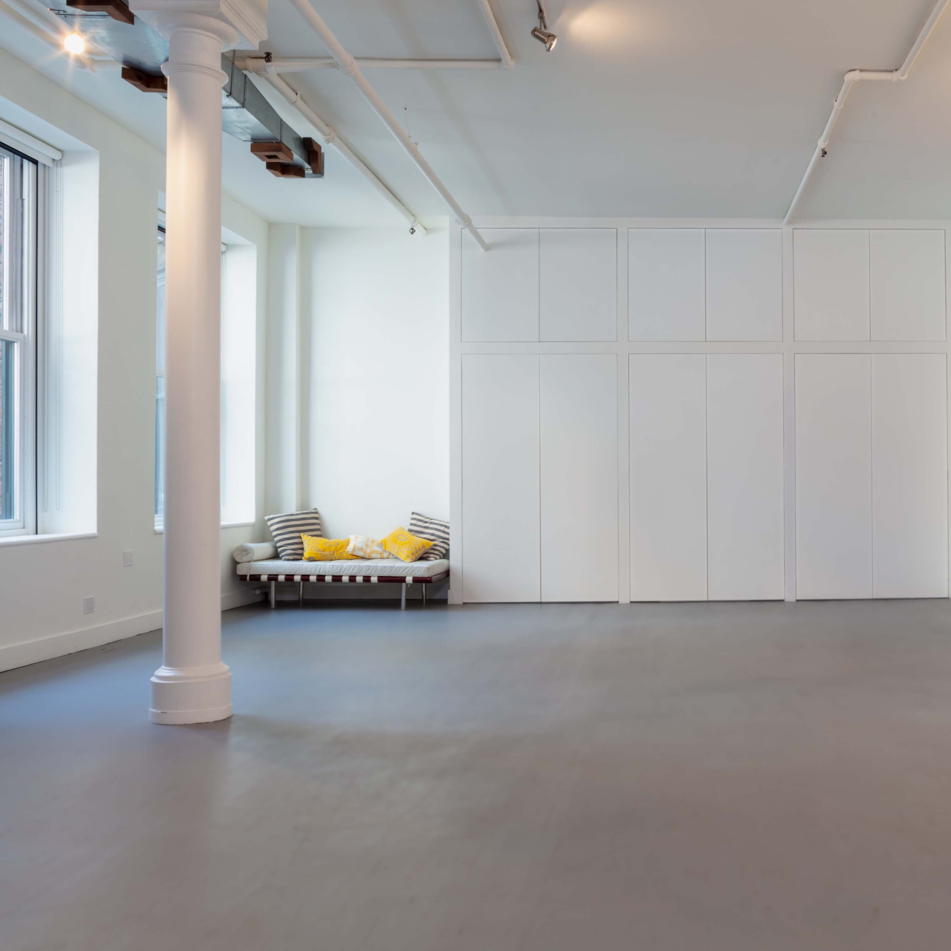 A spacious, minimalist room with a light gray floor, white walls, and a blue archway, featuring a seating area with yellow cushions along one side.