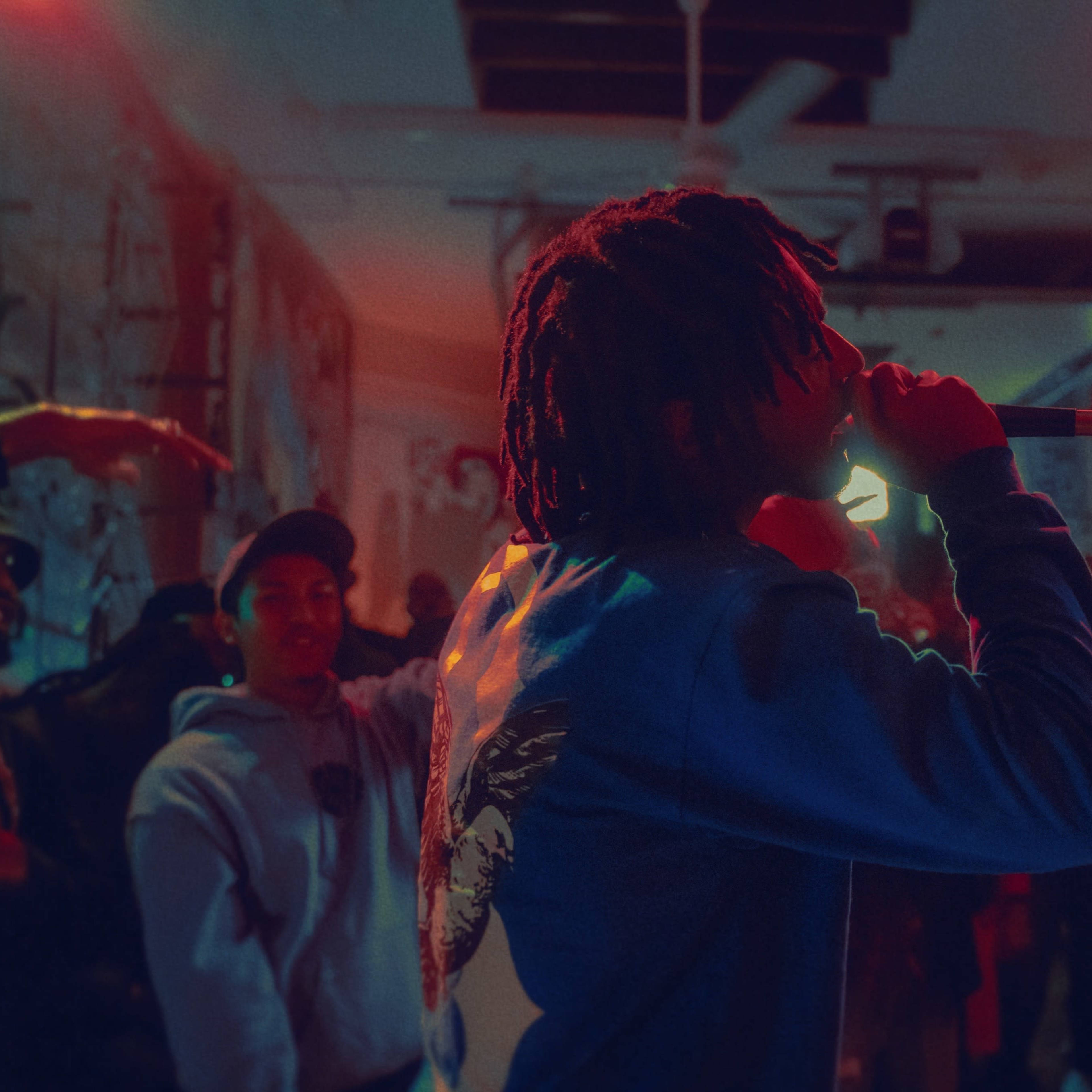 A performer holds a microphone while singing in front of an audience in a vibrant, art-filled venue.