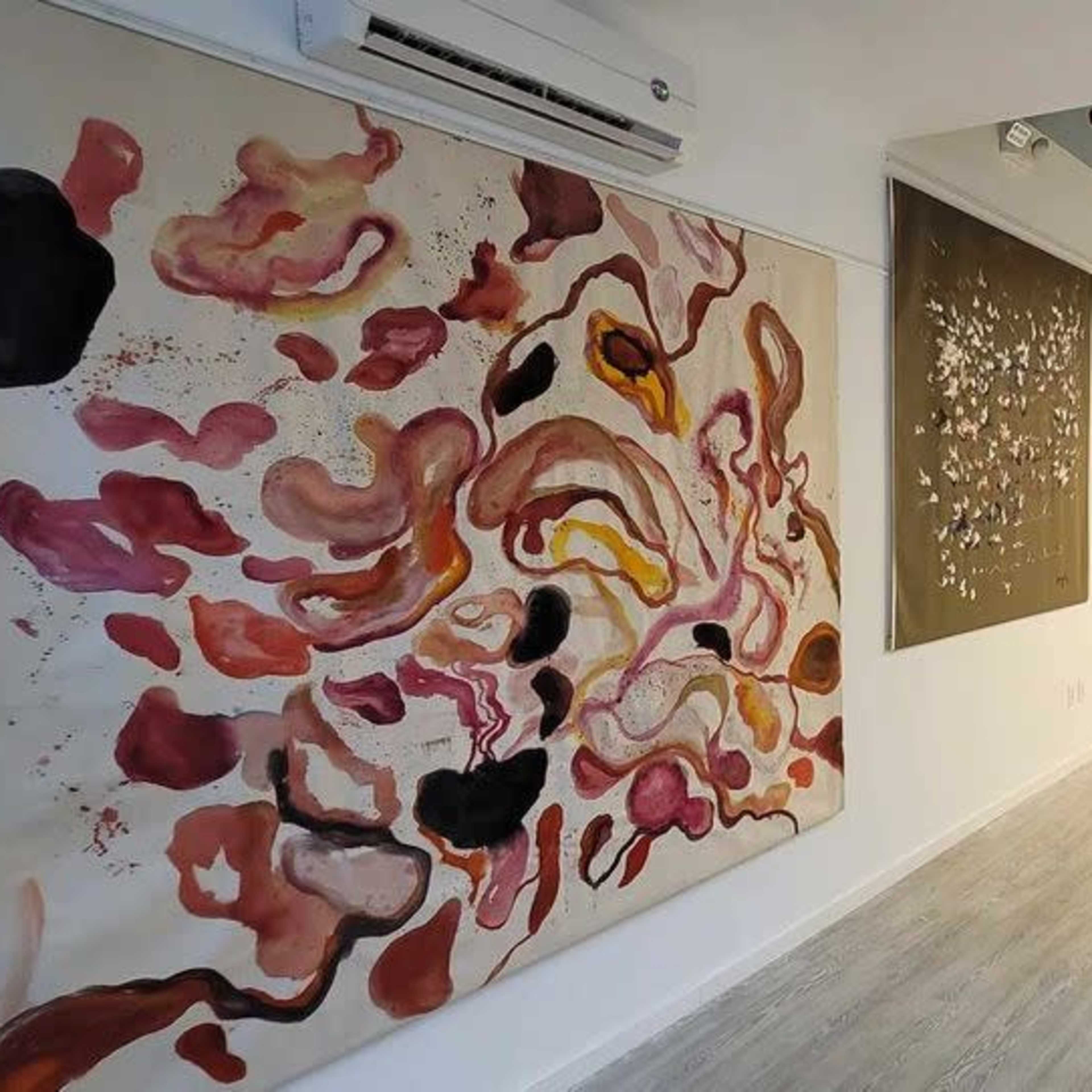 An art gallery featuring several large abstract paintings on the walls, with a light-colored floor and exposed ceiling lights.