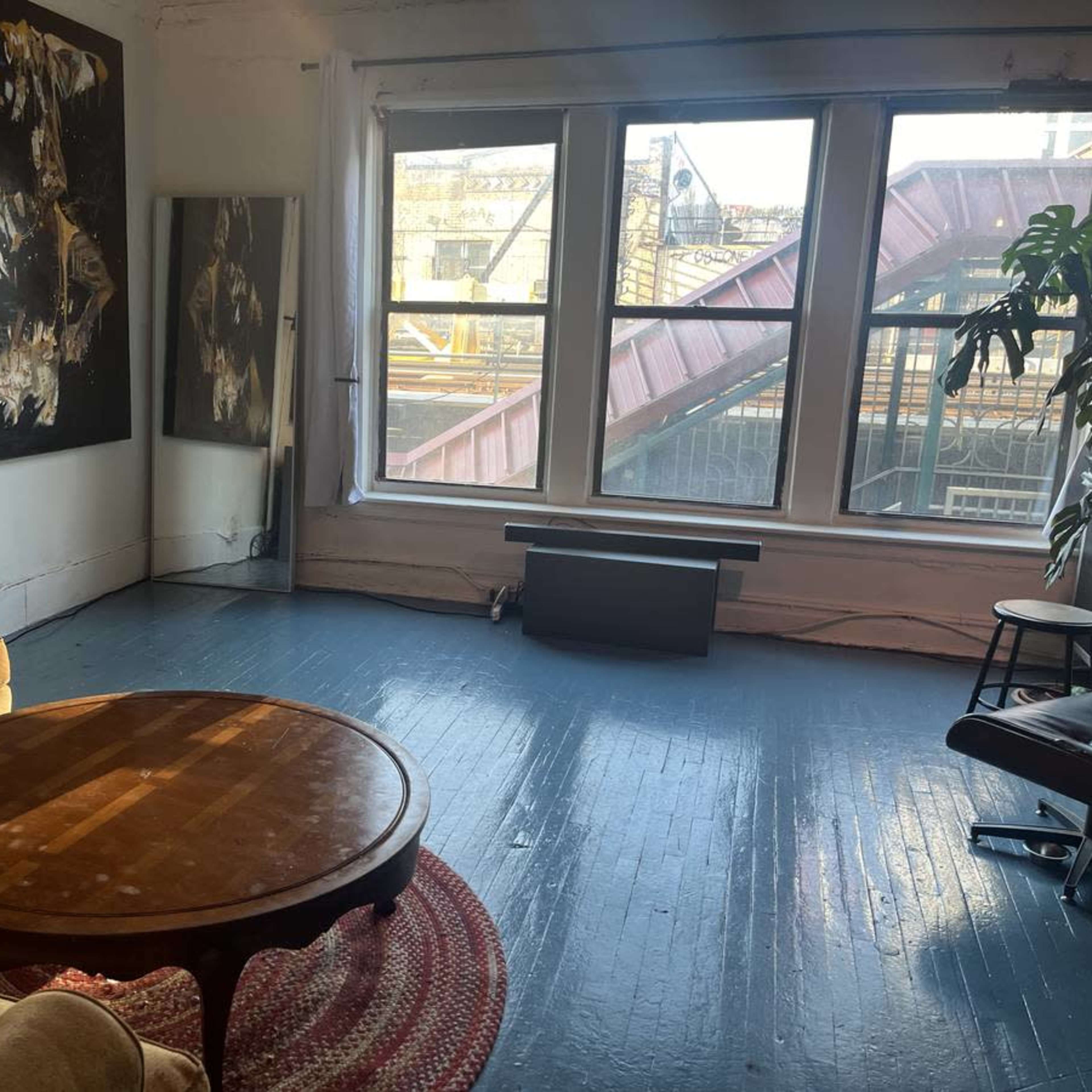 The room features a brown sofa and a circular wooden coffee table, with large windows offering a view of an urban setting.