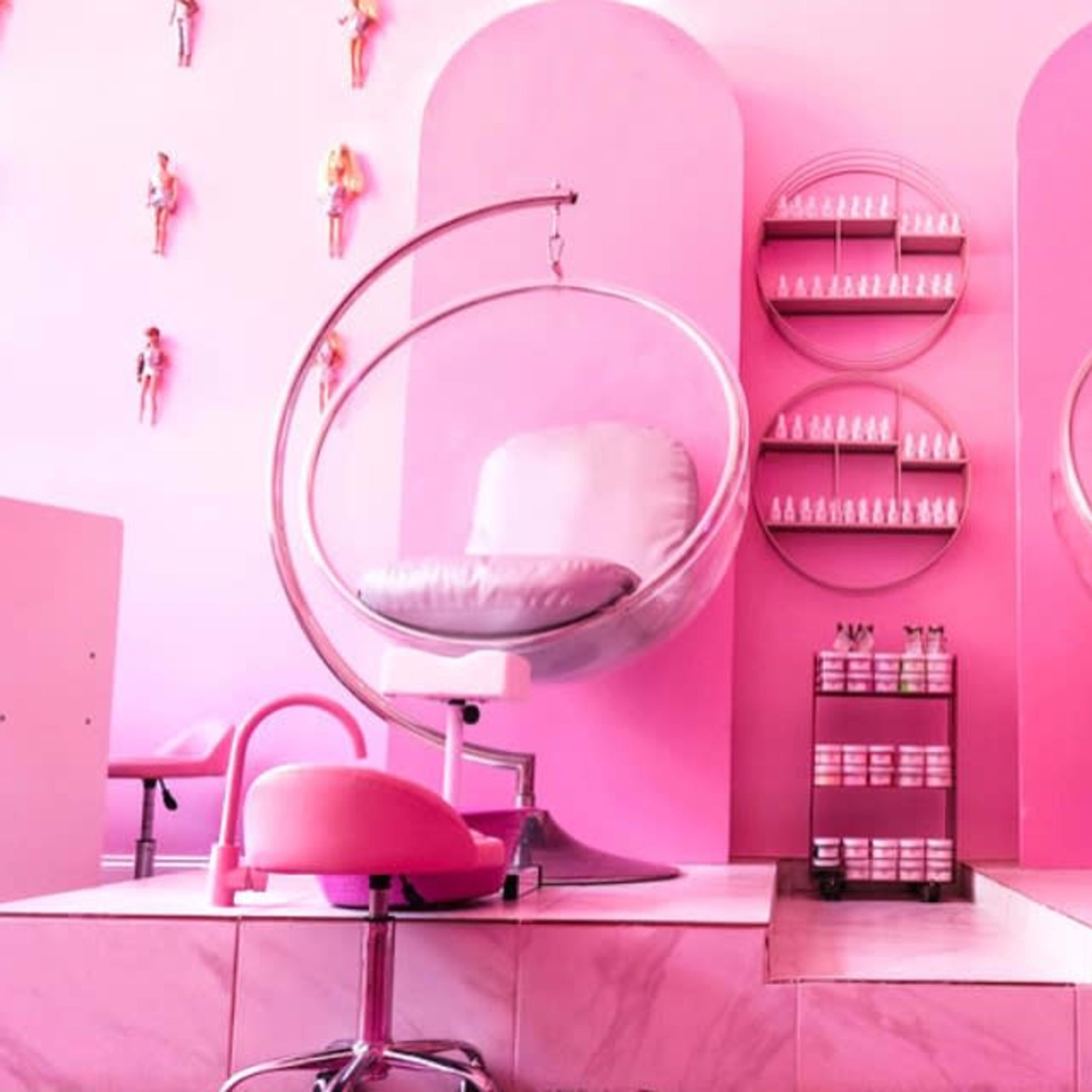 A pink-themed beauty salon with two elegant pedicure chairs, round mirrors, and a display of products on the wall.