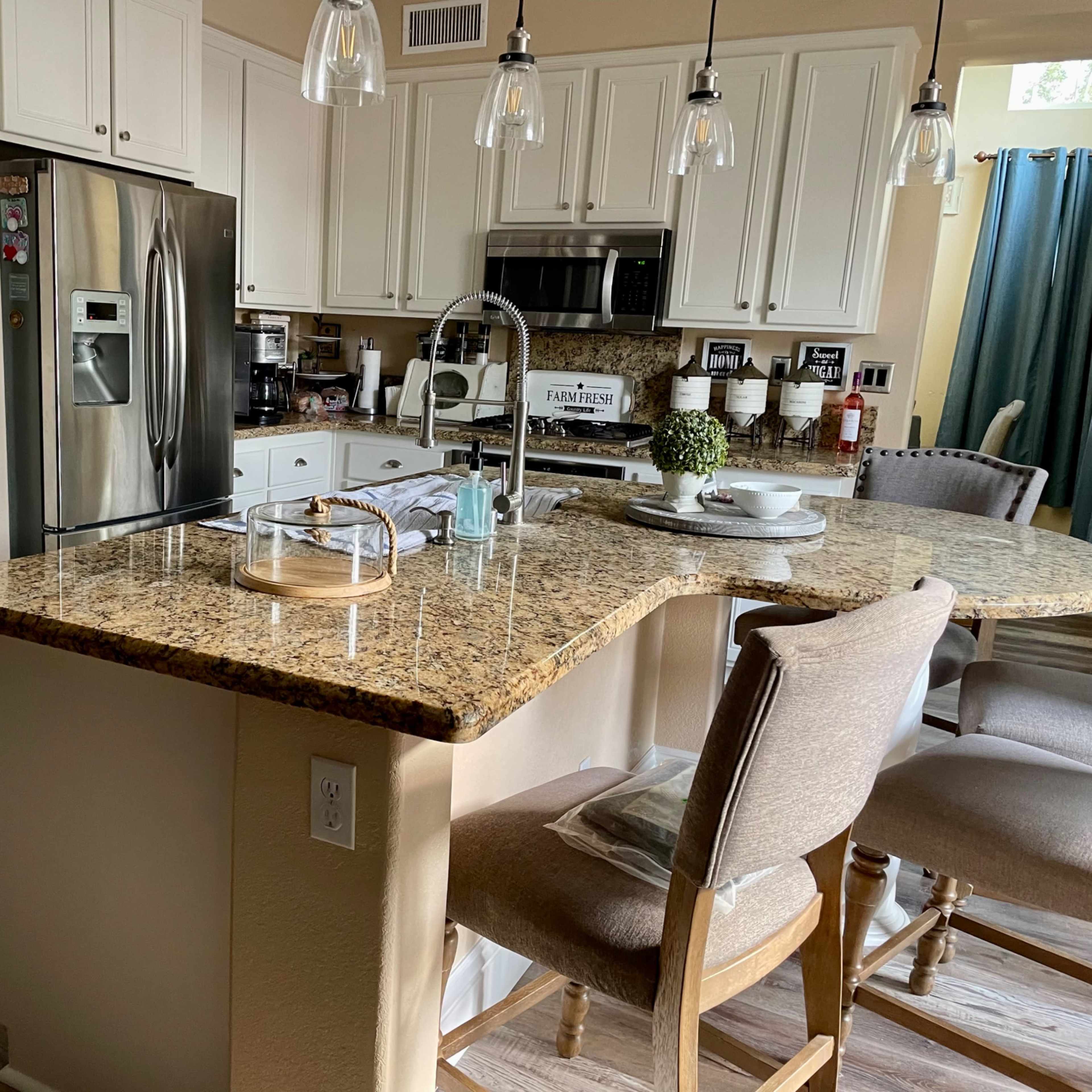 A modern kitchen with white cabinets, stainless steel appliances, a granite countertop, and bar stools.