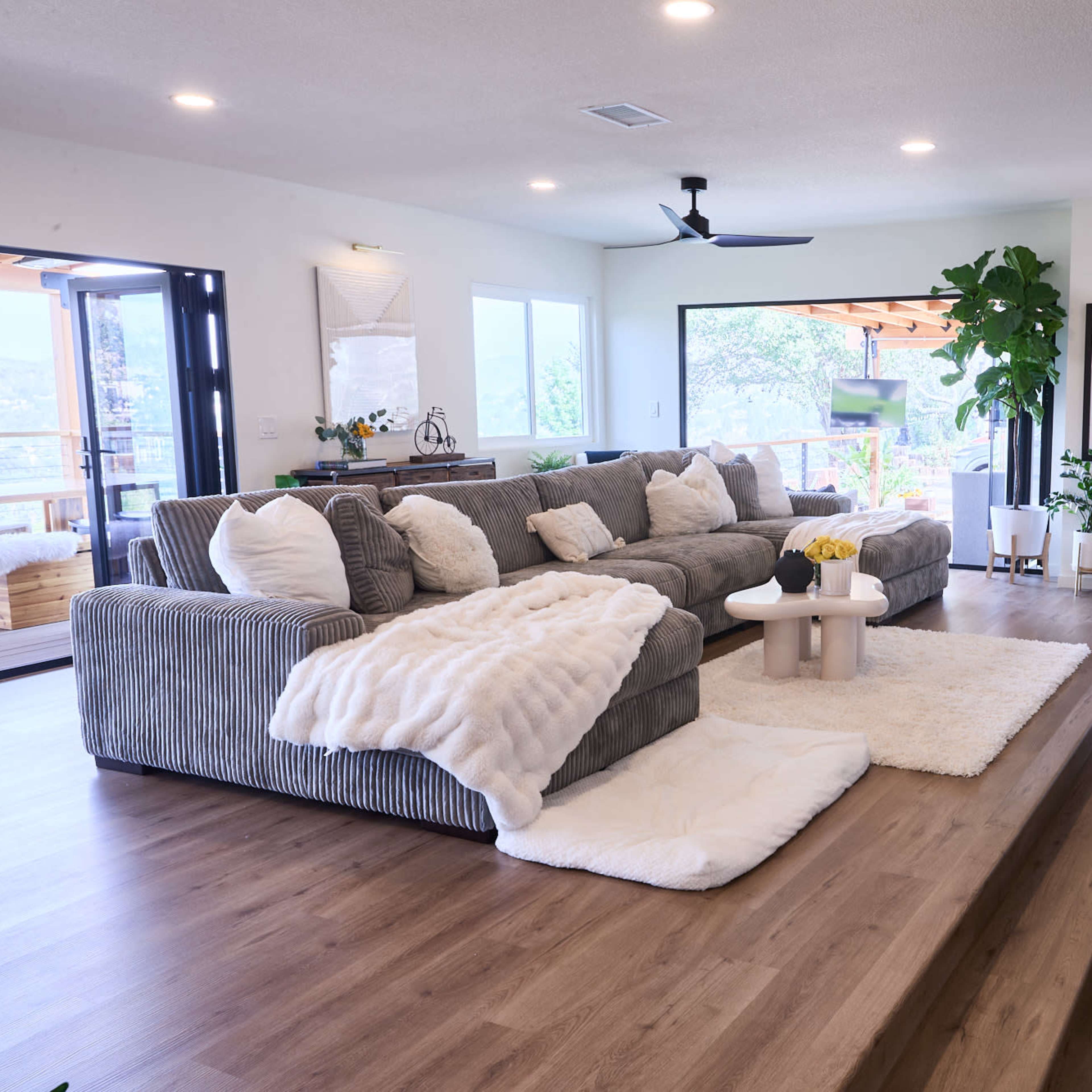 A contemporary living room with a gray sectional sofa, a round white coffee table, and large windows providing a view of the outdoors.