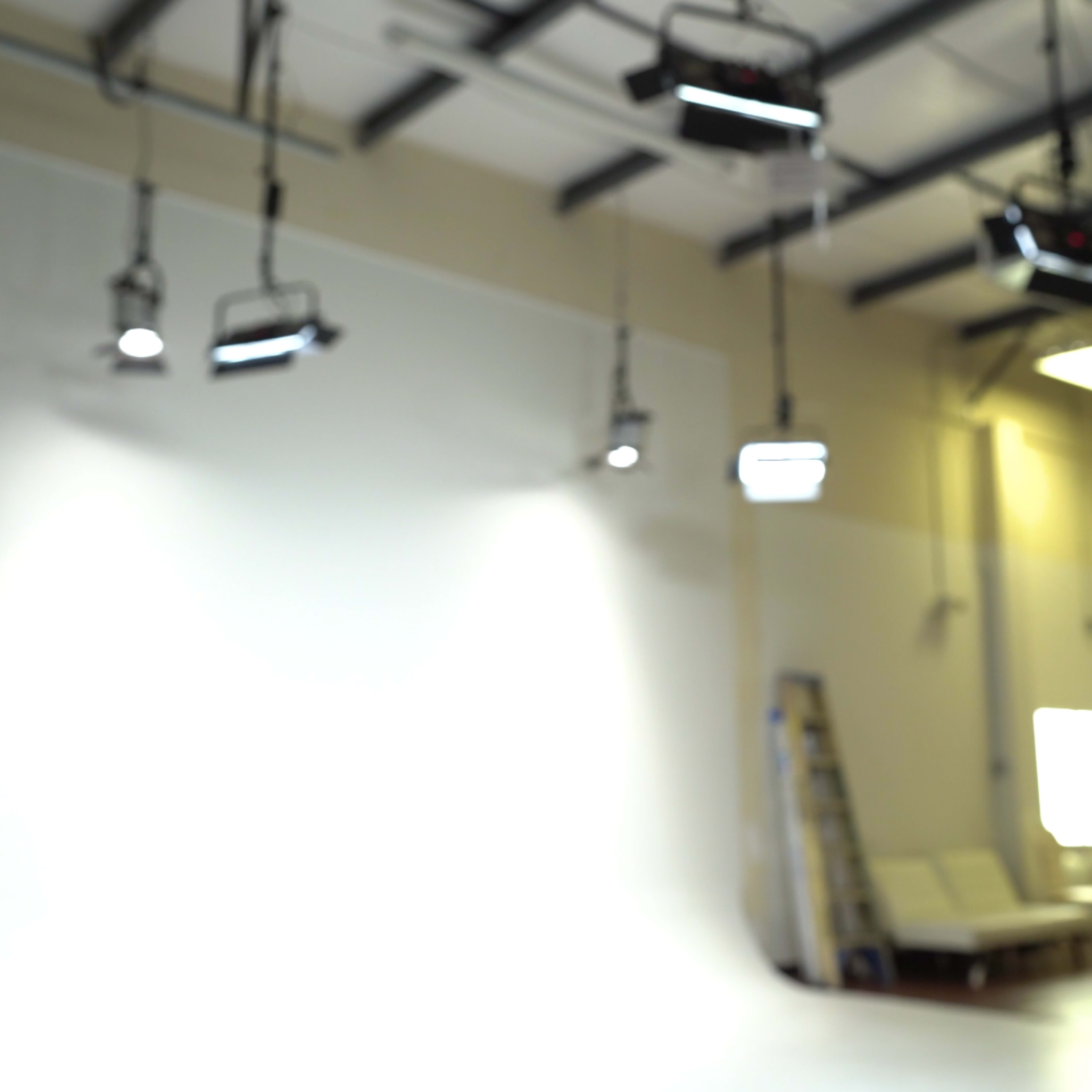 A brightly lit studio with various overhead lights and a white backdrop.