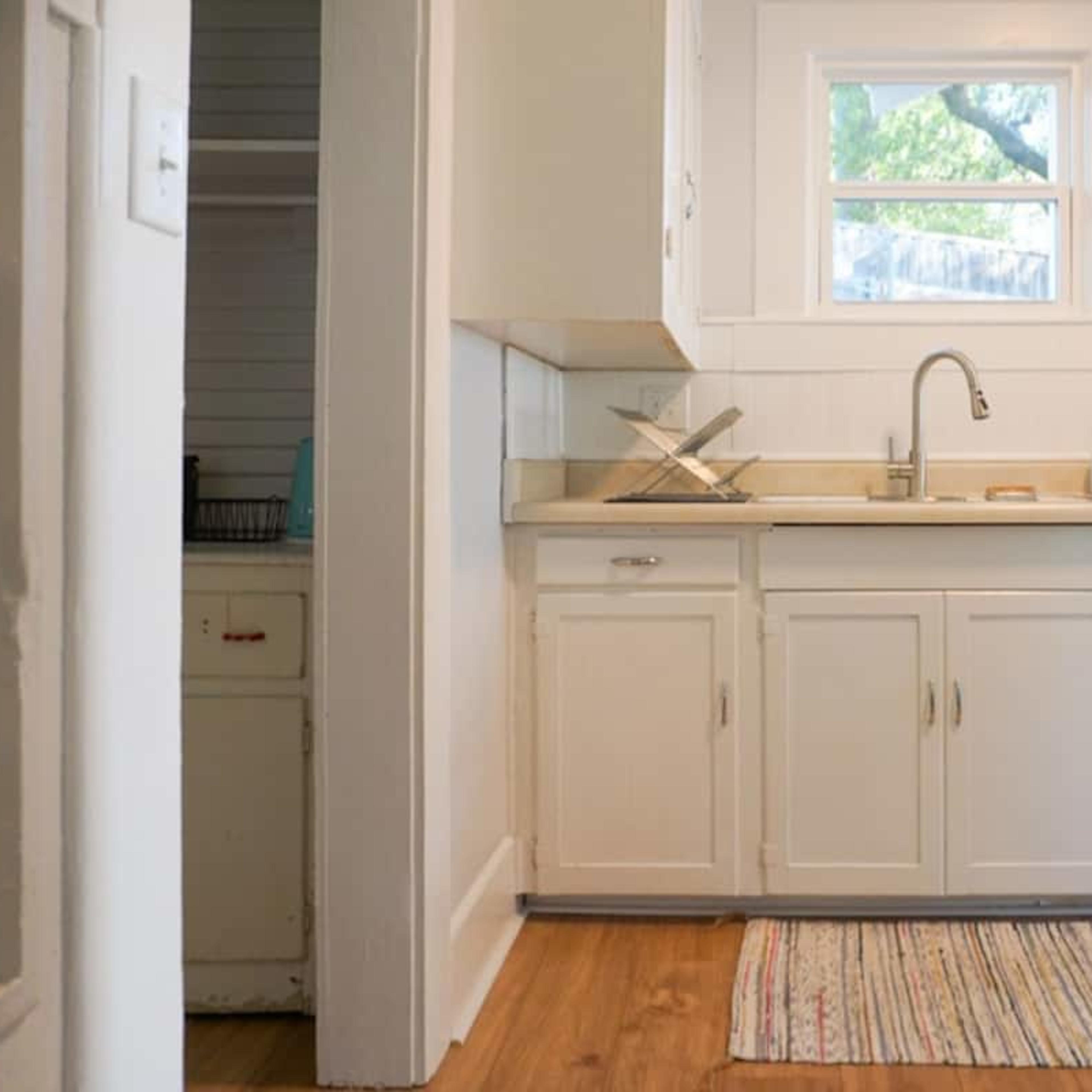 A small kitchen with white cabinetry, a sink, and a blue refrigerator, featuring a striped rug on the wooden floor.