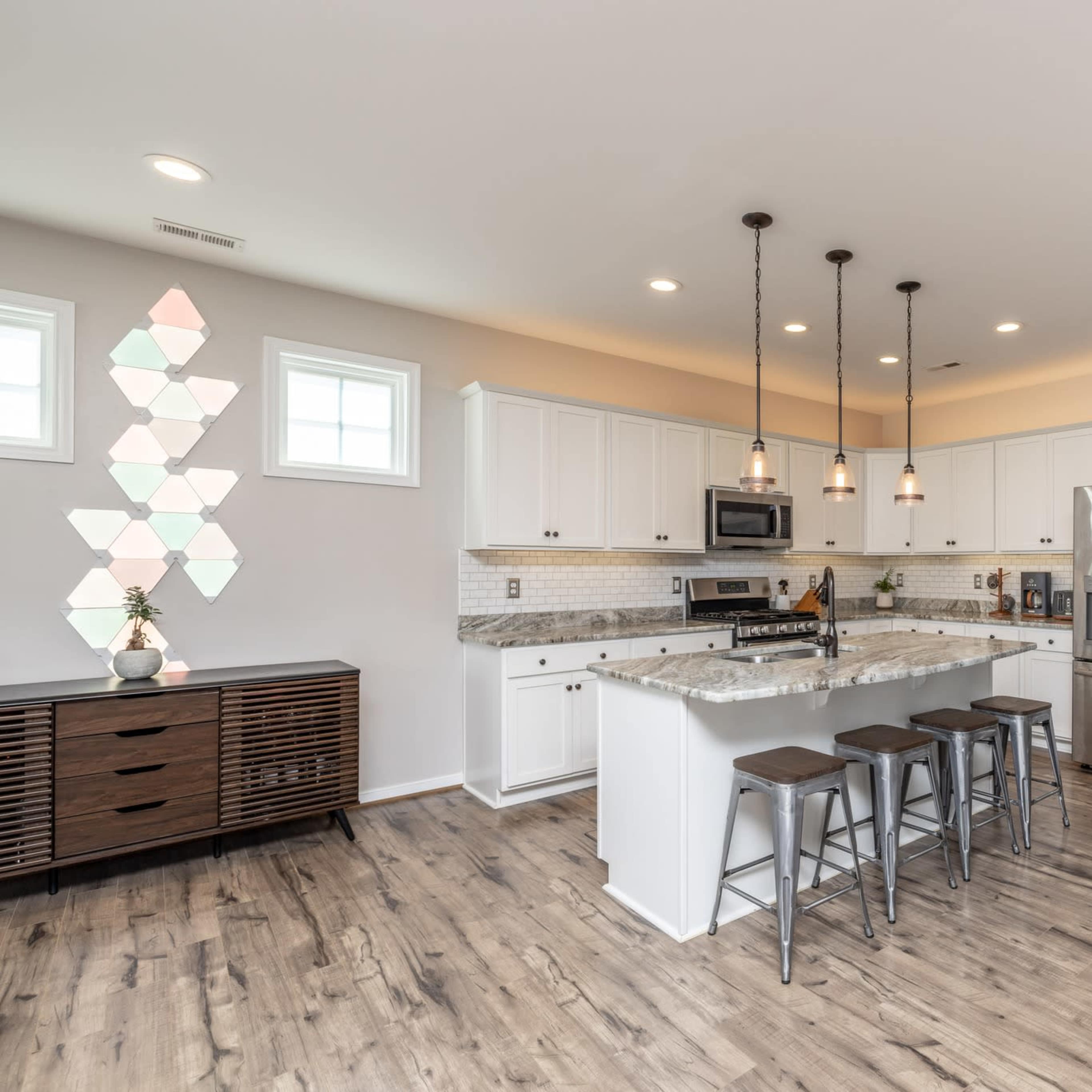 A modern kitchen with white cabinetry, stainless steel appliances, a marble-topped island, and wooden flooring.