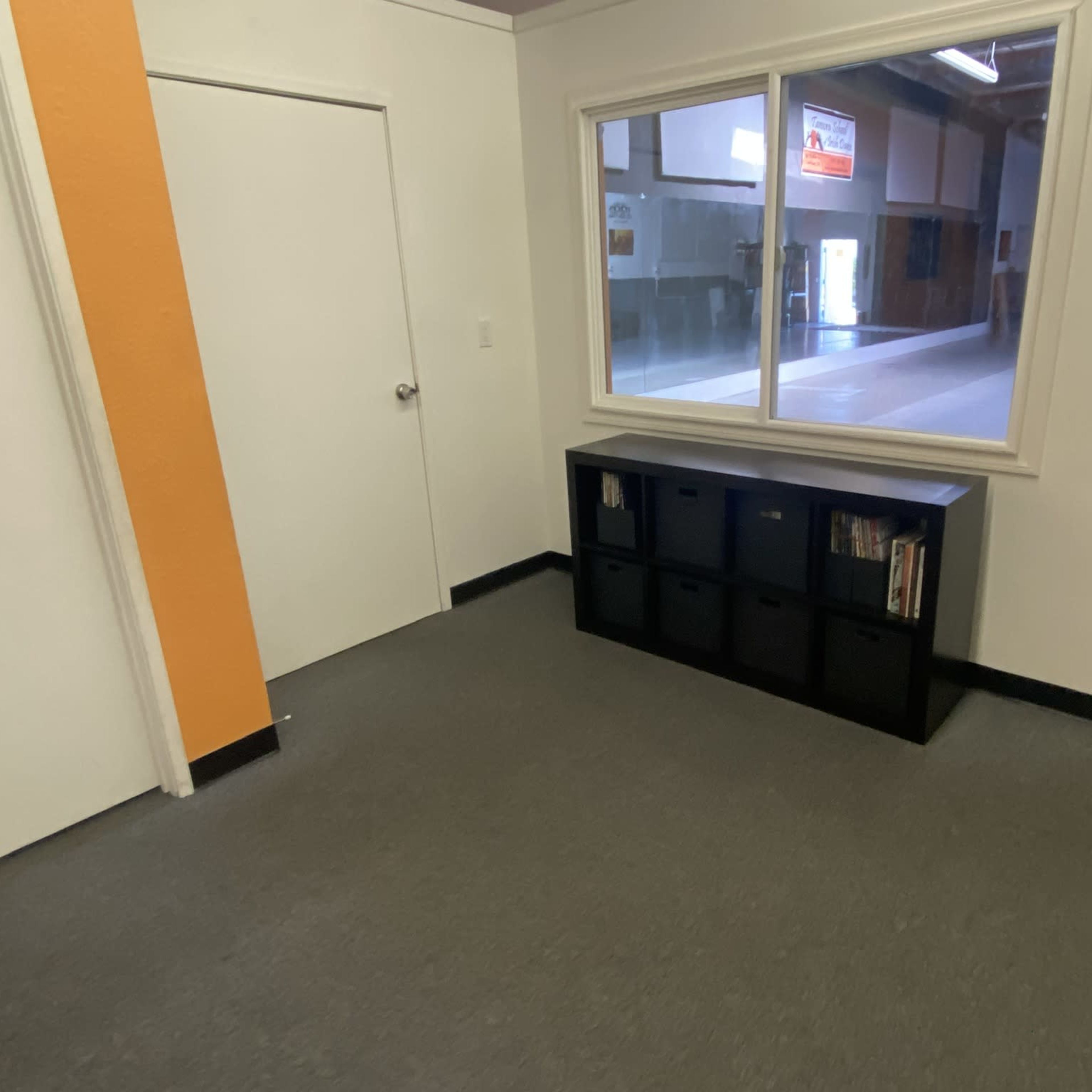 A hallway features a door, a large window, and a black storage unit against the wall.
