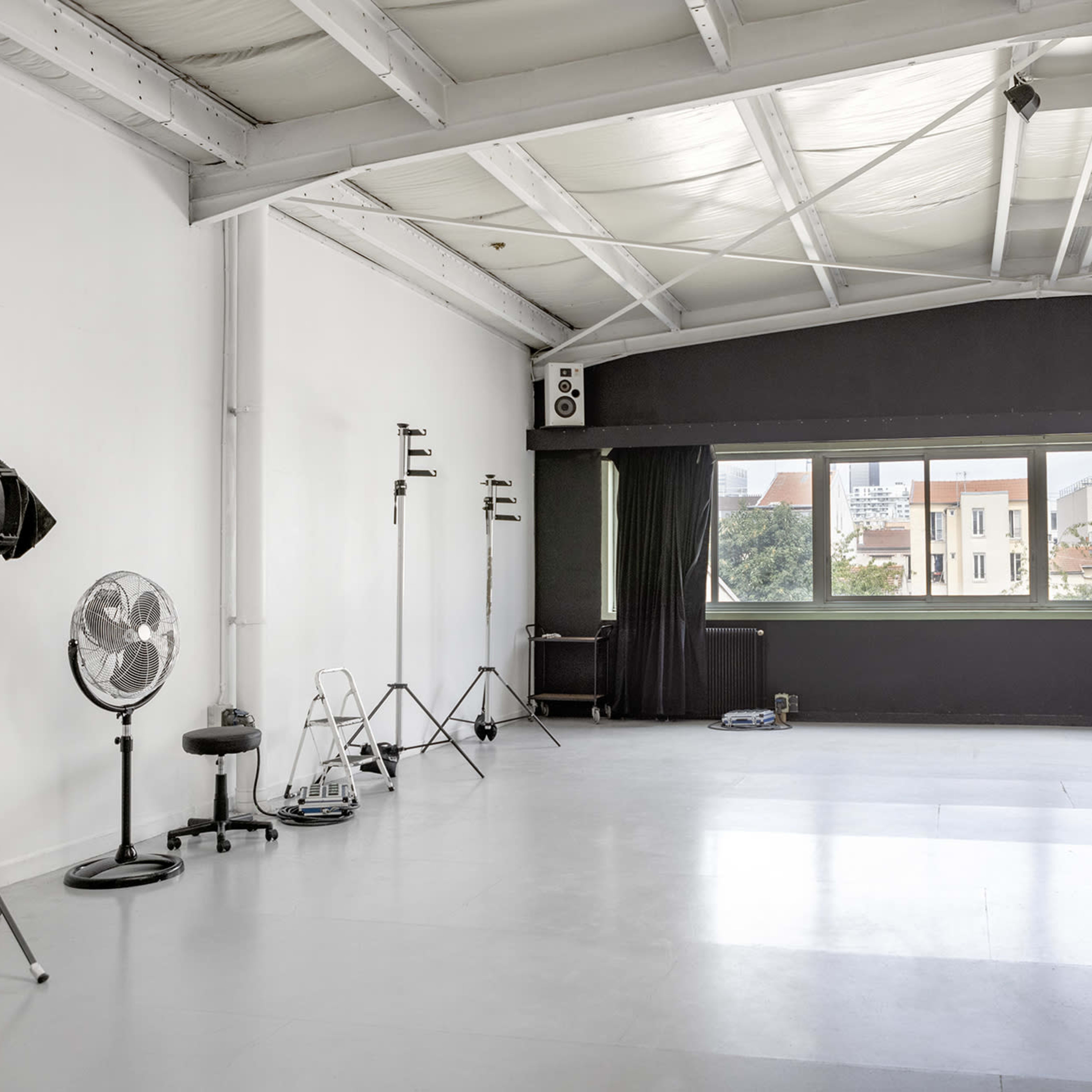 A spacious, minimally furnished photography studio with large windows and various equipment arranged along the walls.