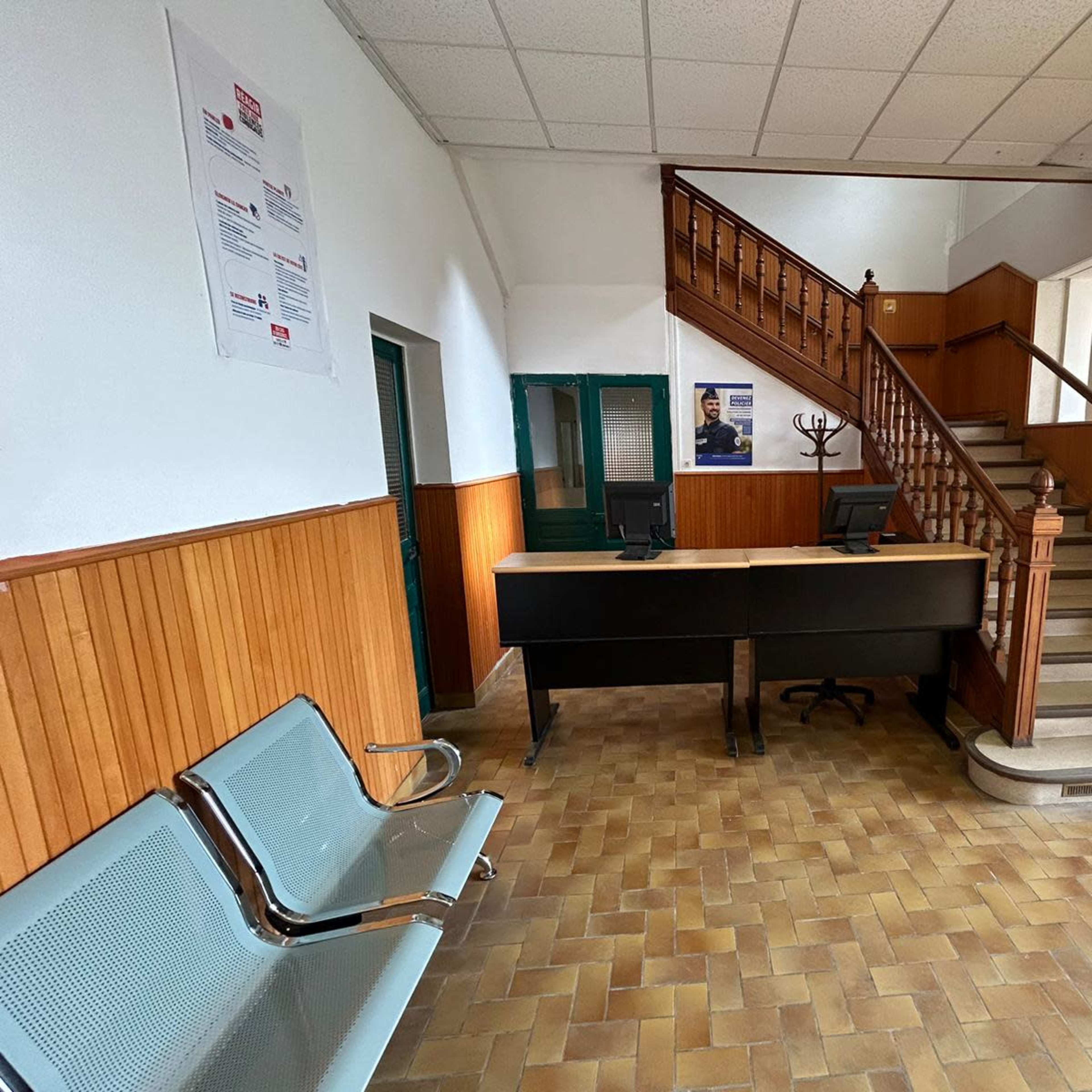A spacious reception area with a front desk and a staircase leading to an upper level, flanked by seating and wooden paneling on the walls.
