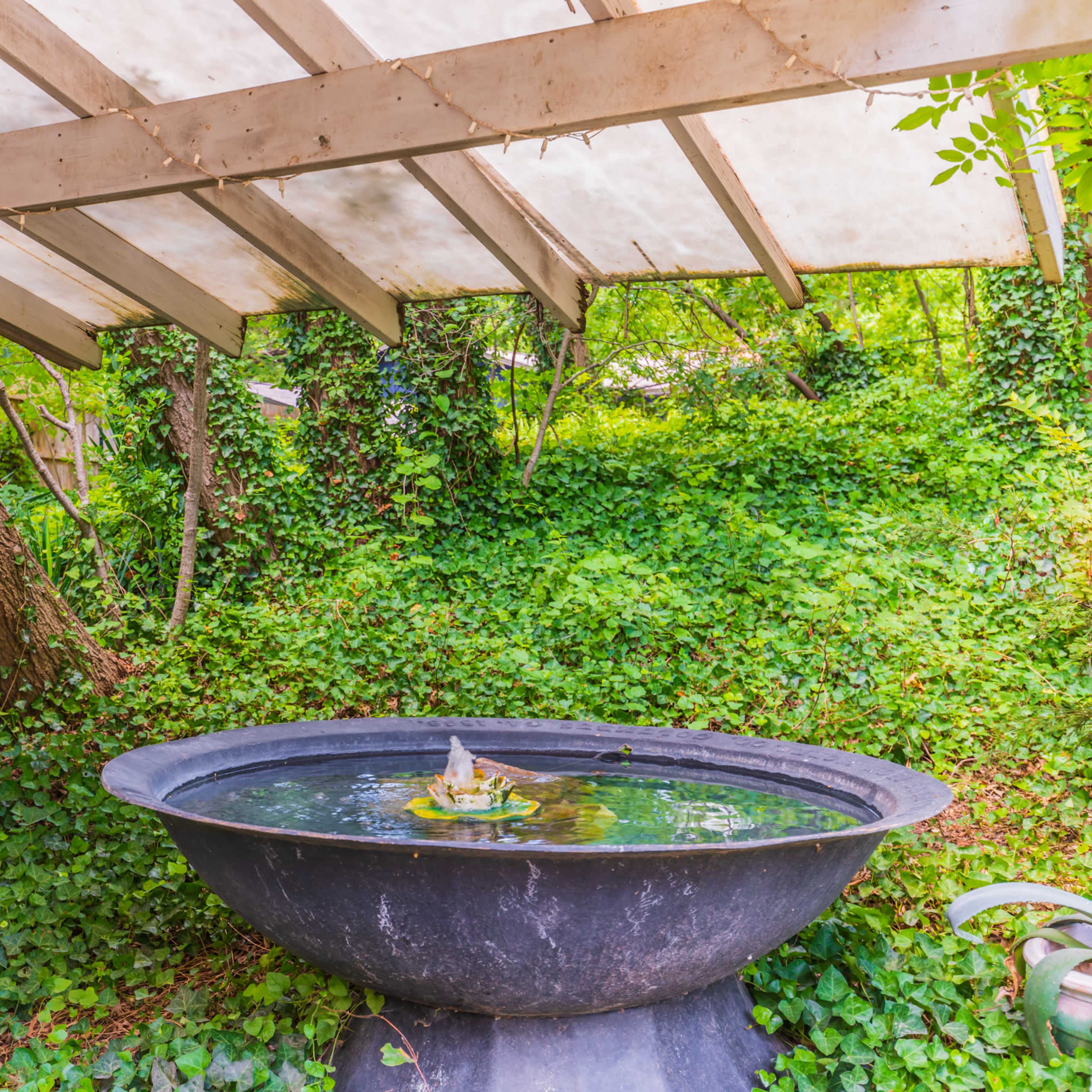 A circular fountain surrounded by lush green ivy under a wooden structure with a slanted roof.