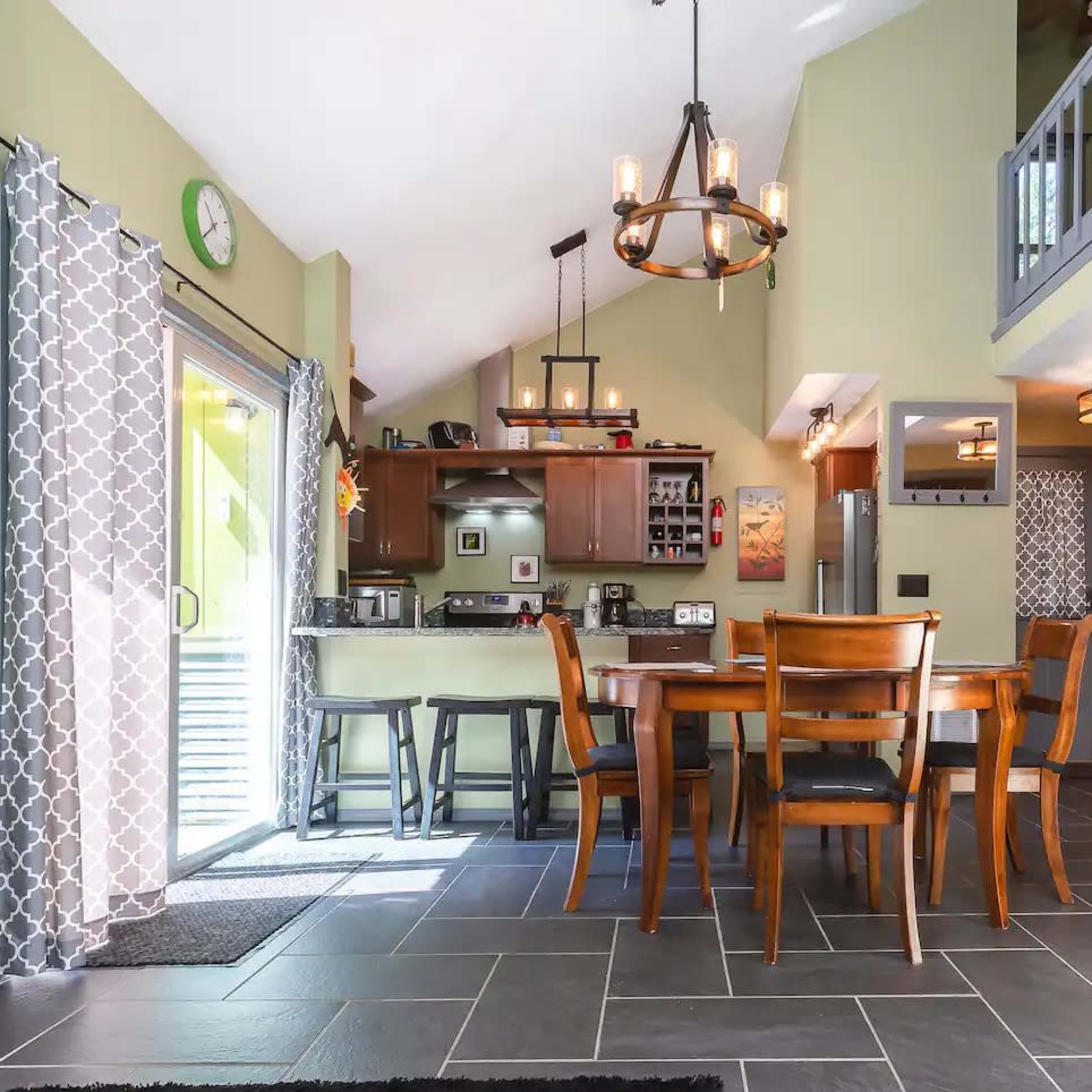 An open-concept living and dining area with a kitchen, featuring tile flooring, a wooden dining table, and large windows.