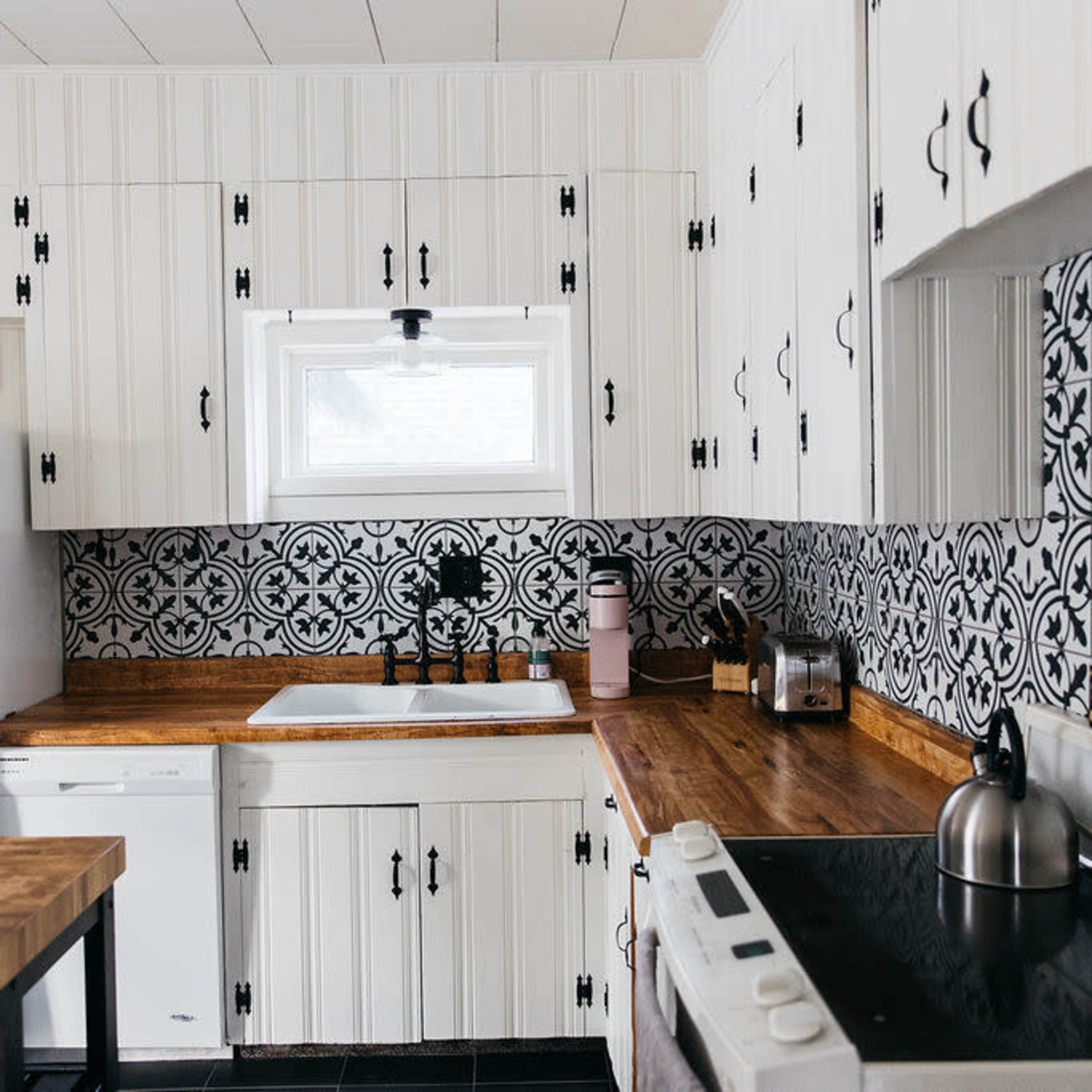 A modern kitchen featuring white cabinetry, a patterned black and white backsplash, and wooden countertops.