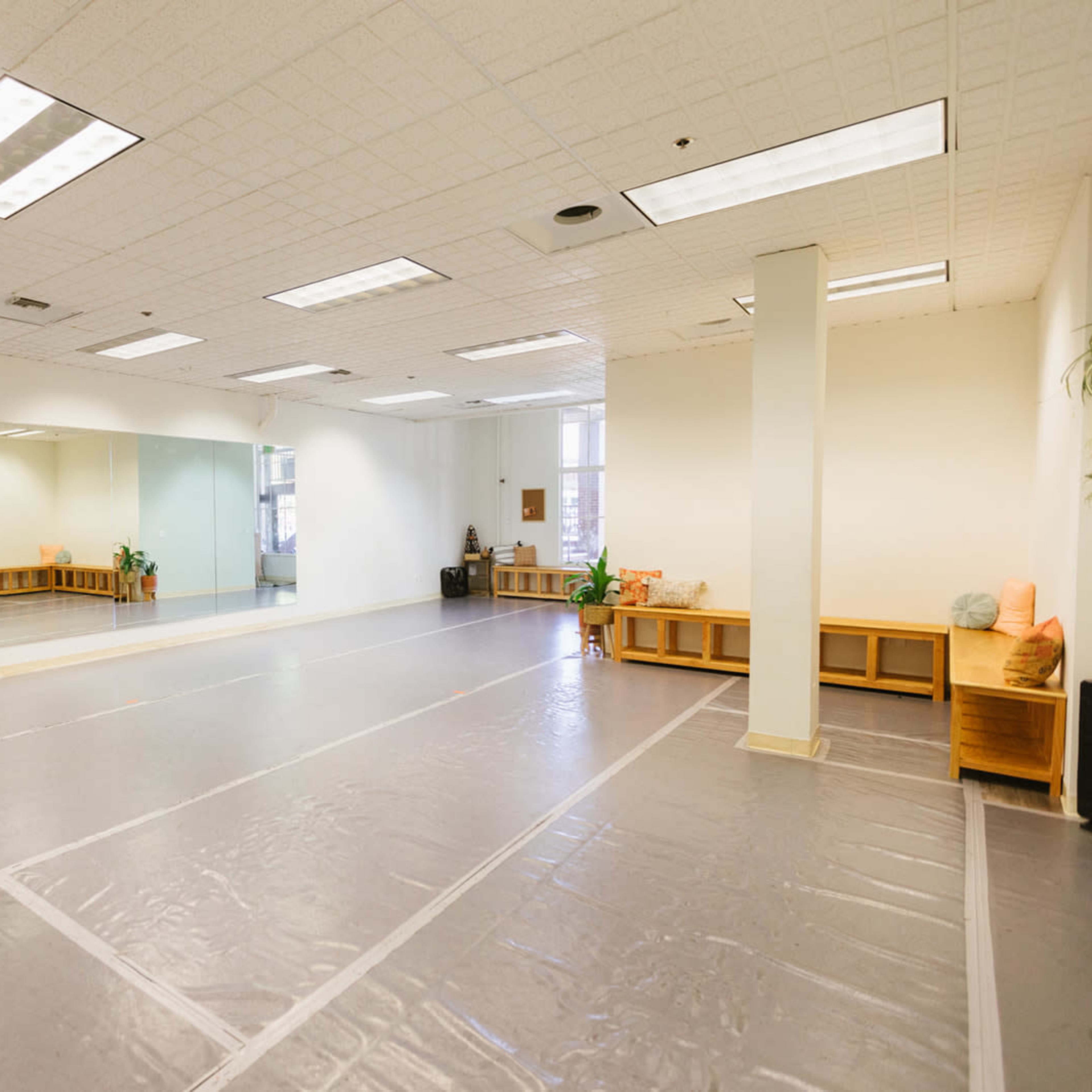 A spacious, empty studio with a mirrored wall, hardwood floors, and soft lighting.