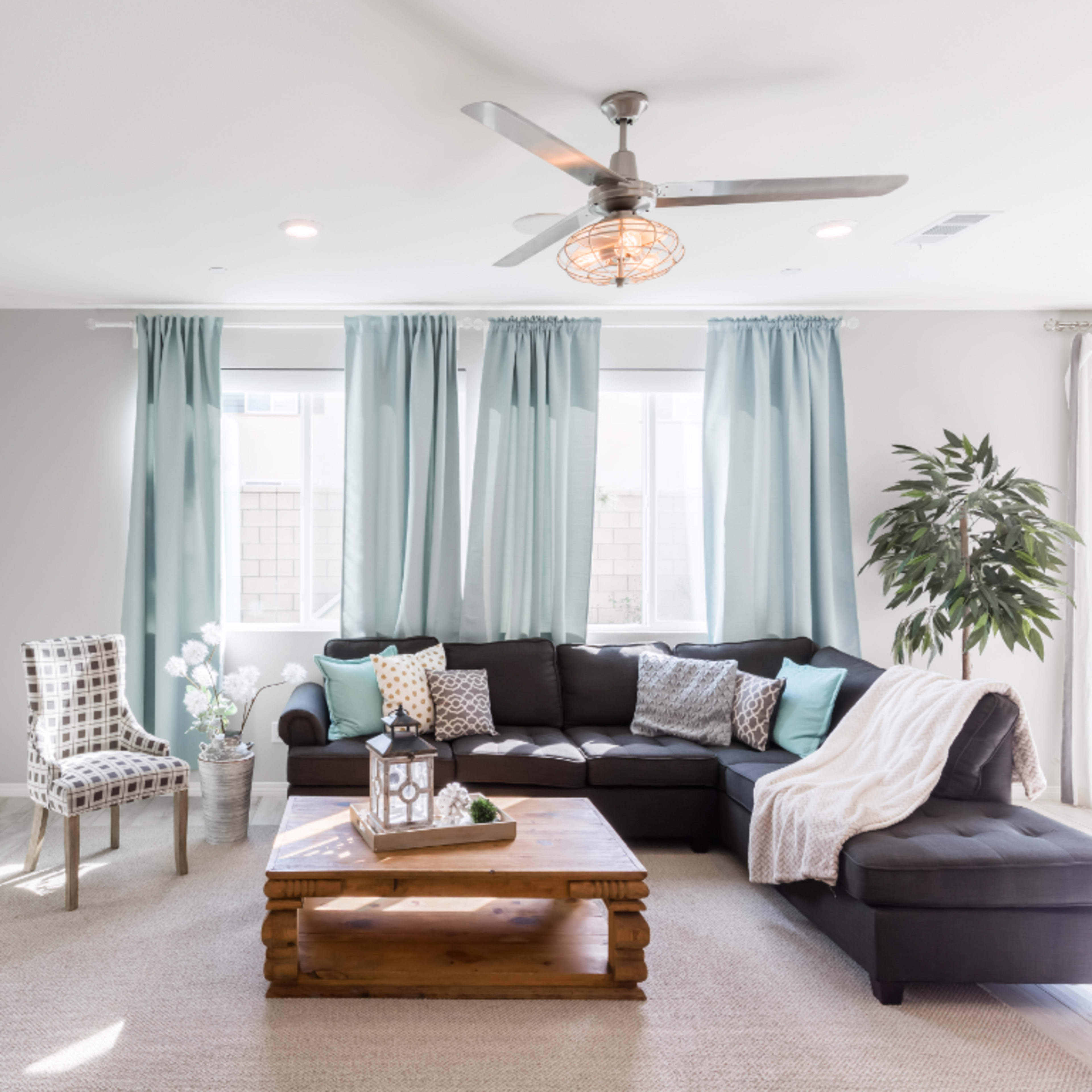 A modern living room features a sectional sofa, a wooden coffee table, a fireplace, and large windows with light blue curtains.