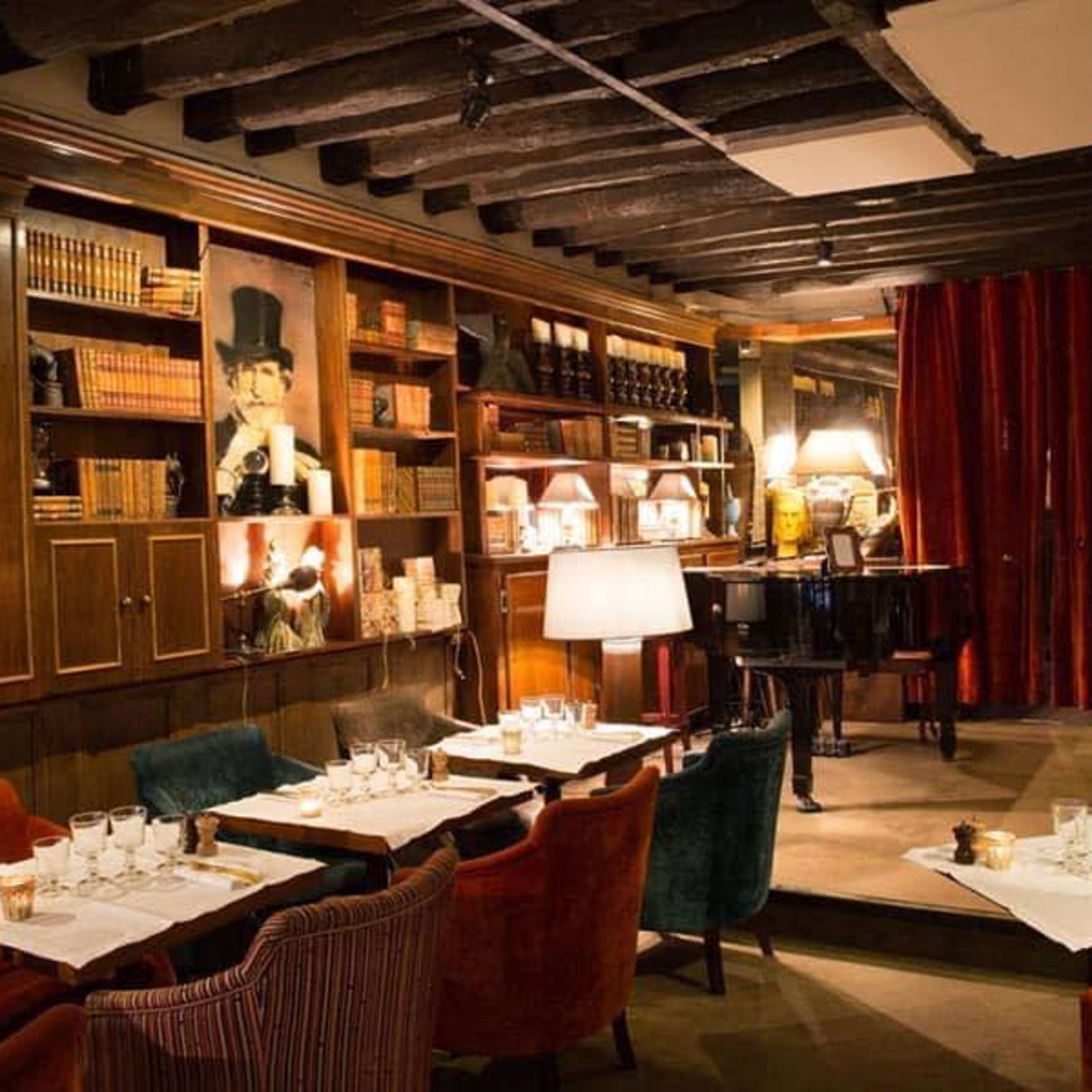 A cozy restaurant interior with wooden beams, tables set with white tablecloths, and bookshelves filled with books.