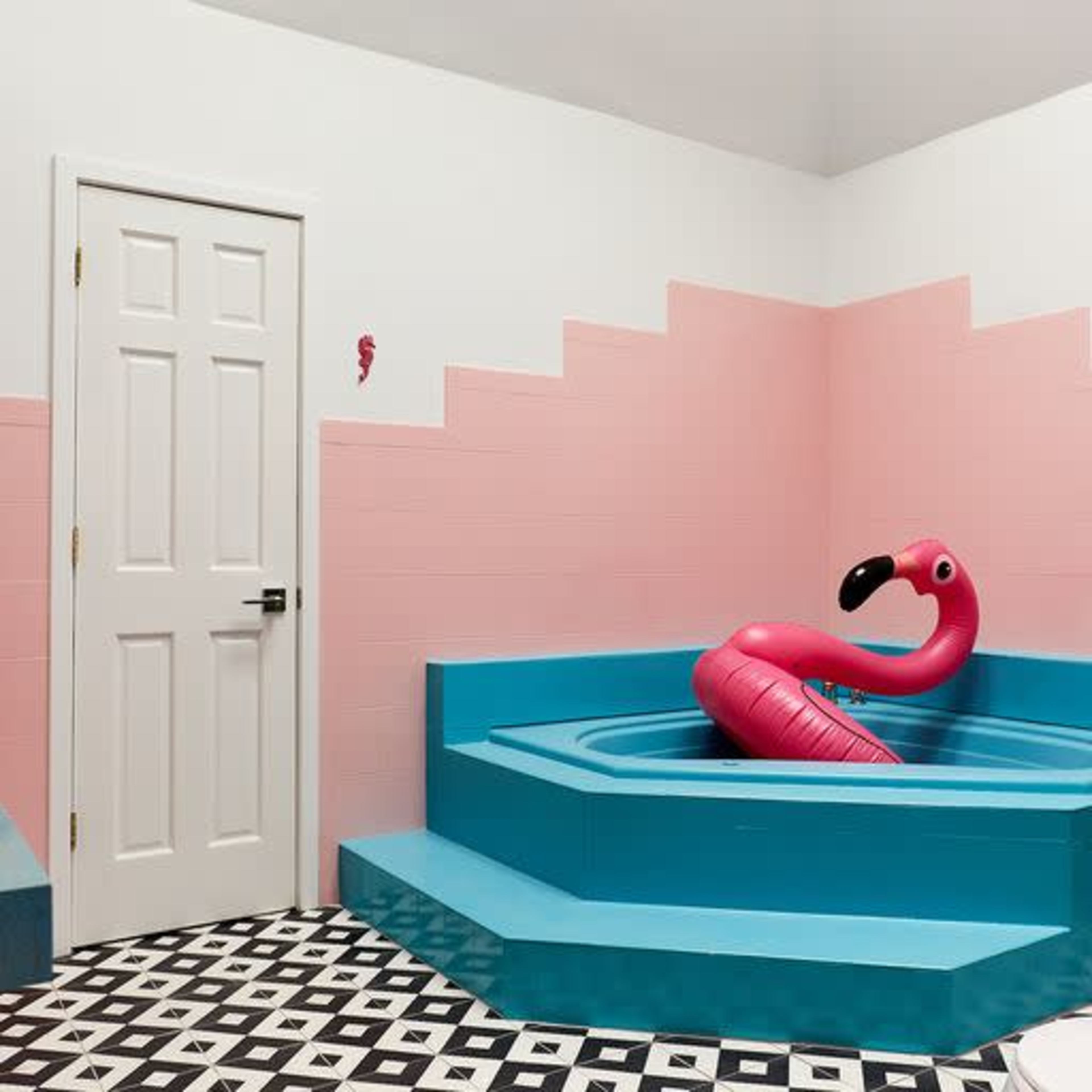 A brightly colored bathroom featuring a turquoise bathtub shaped like a flamingo and pink walls with a black and white tiled floor.