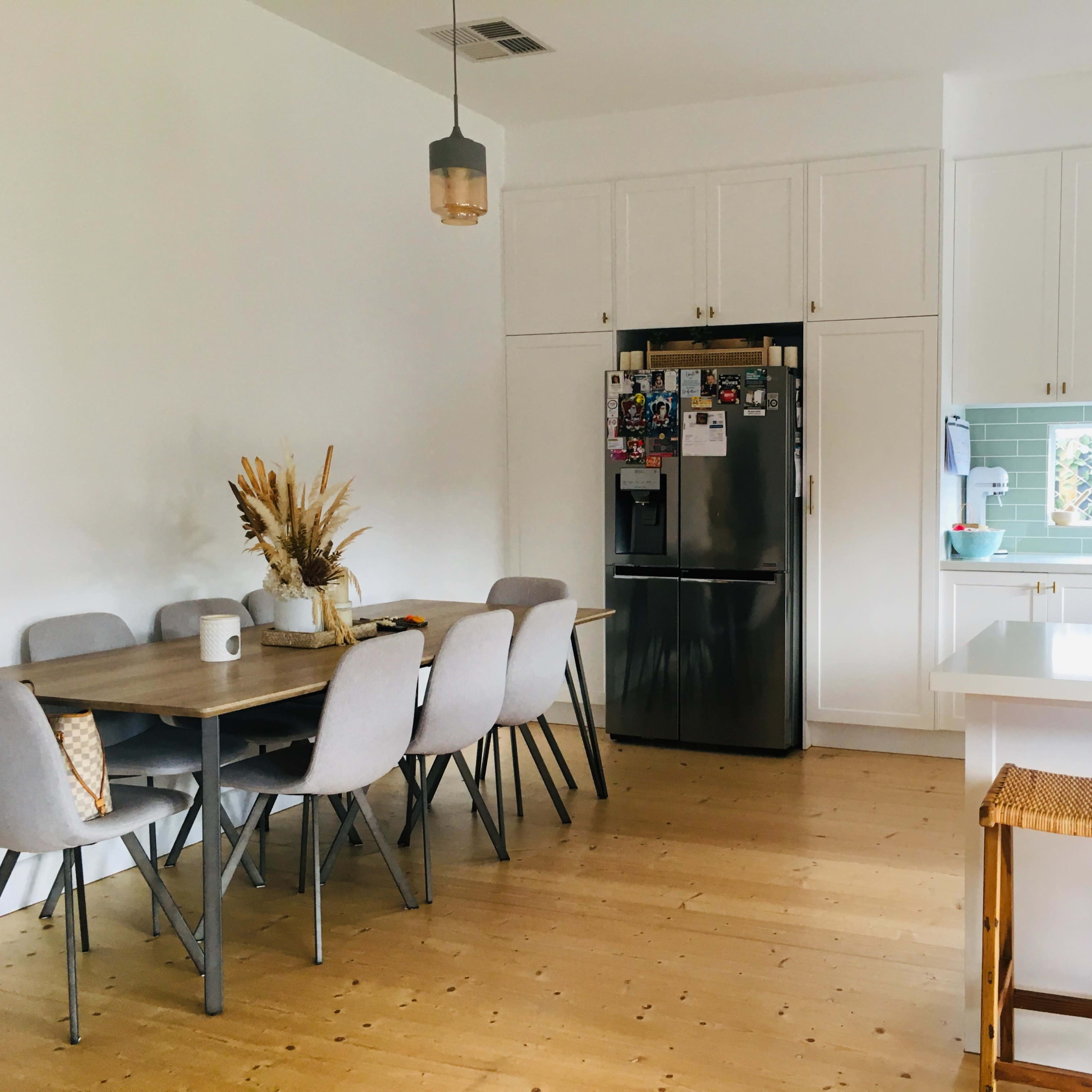 A kitchen and dining area features a table with six chairs, a refrigerator, and a stove, with natural light illuminating the space.