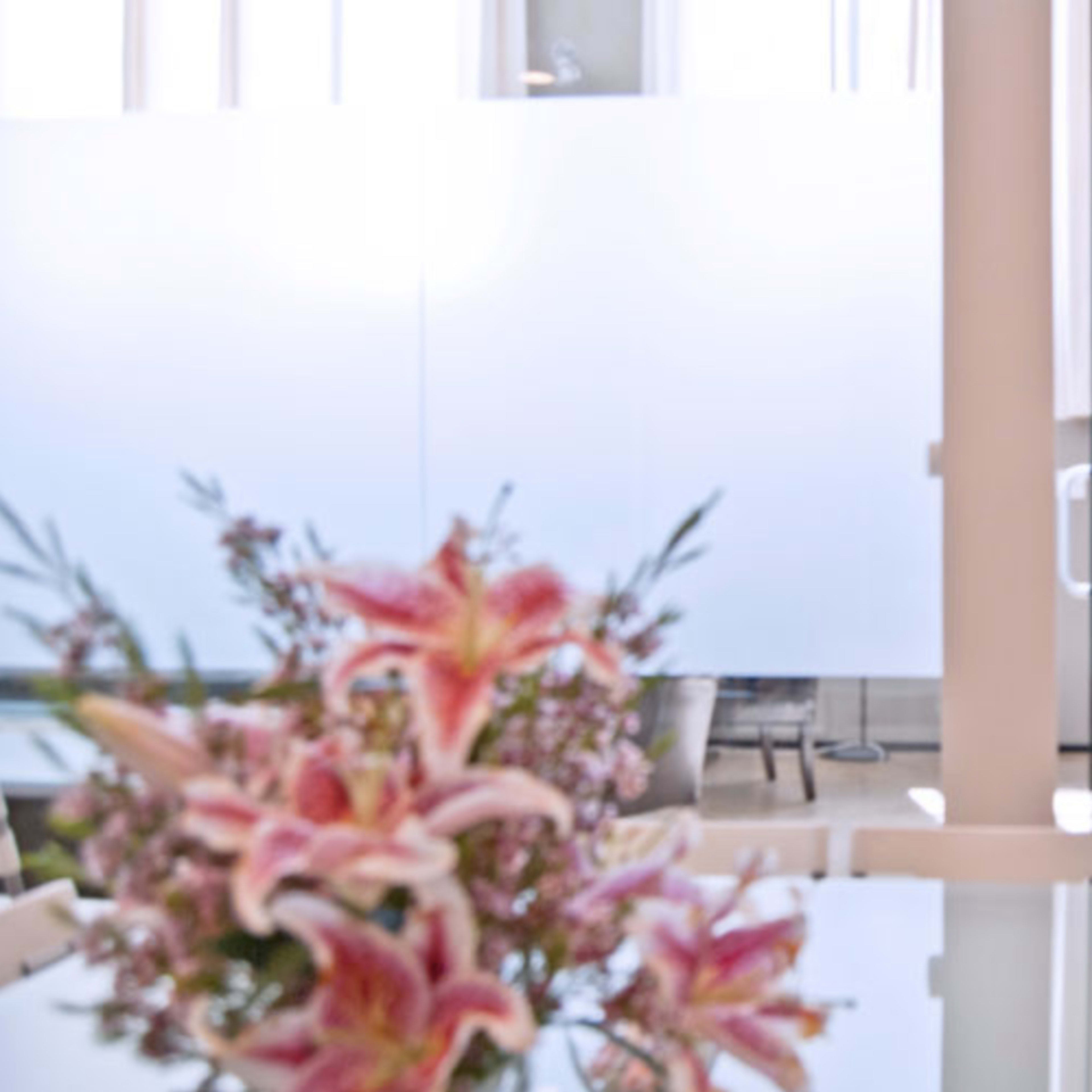 A modern office interior with a glass partition, a staircase, and a table with a vase of flowers.