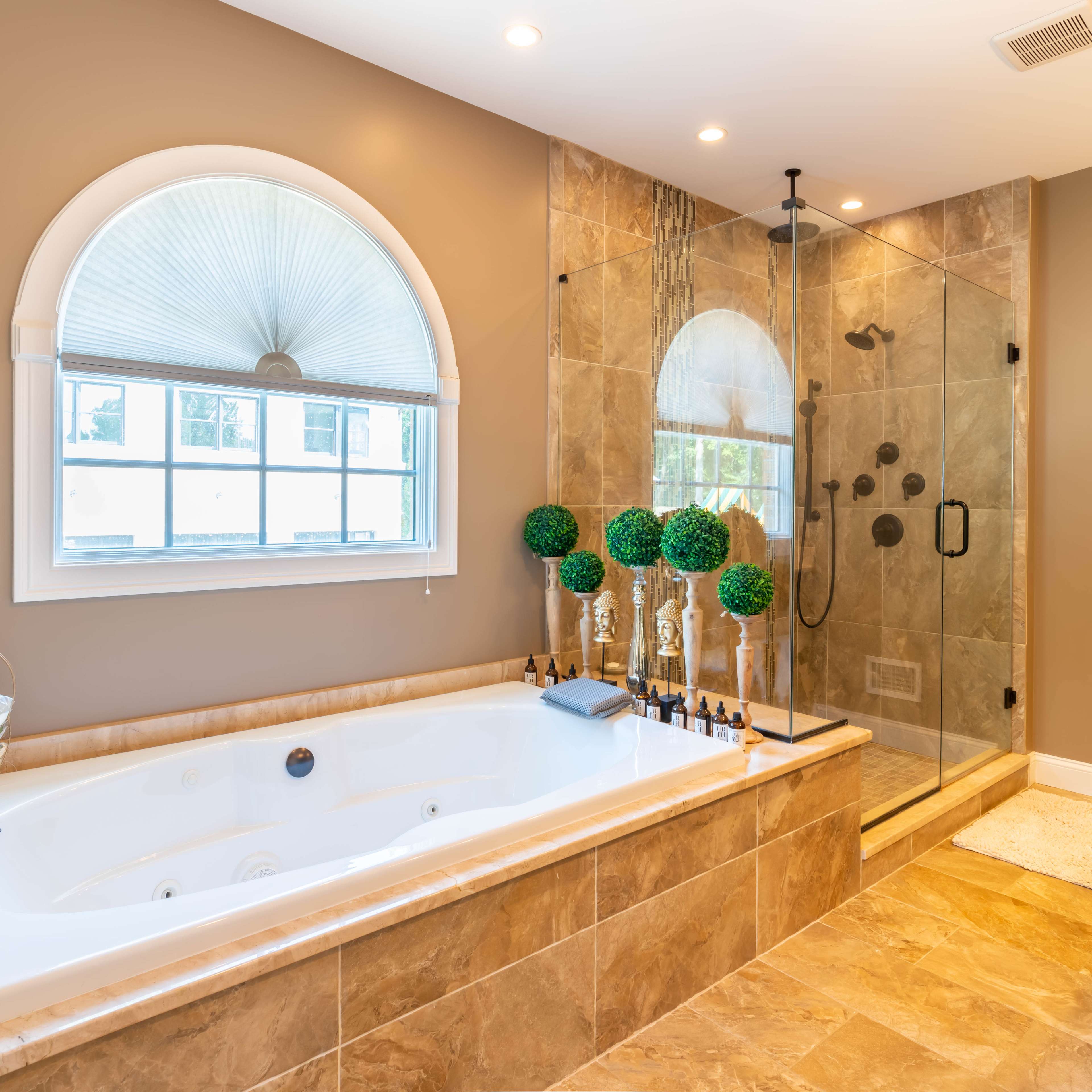 The bathroom features a large bathtub beside a glass shower enclosure with decorative plants and dual sinks.