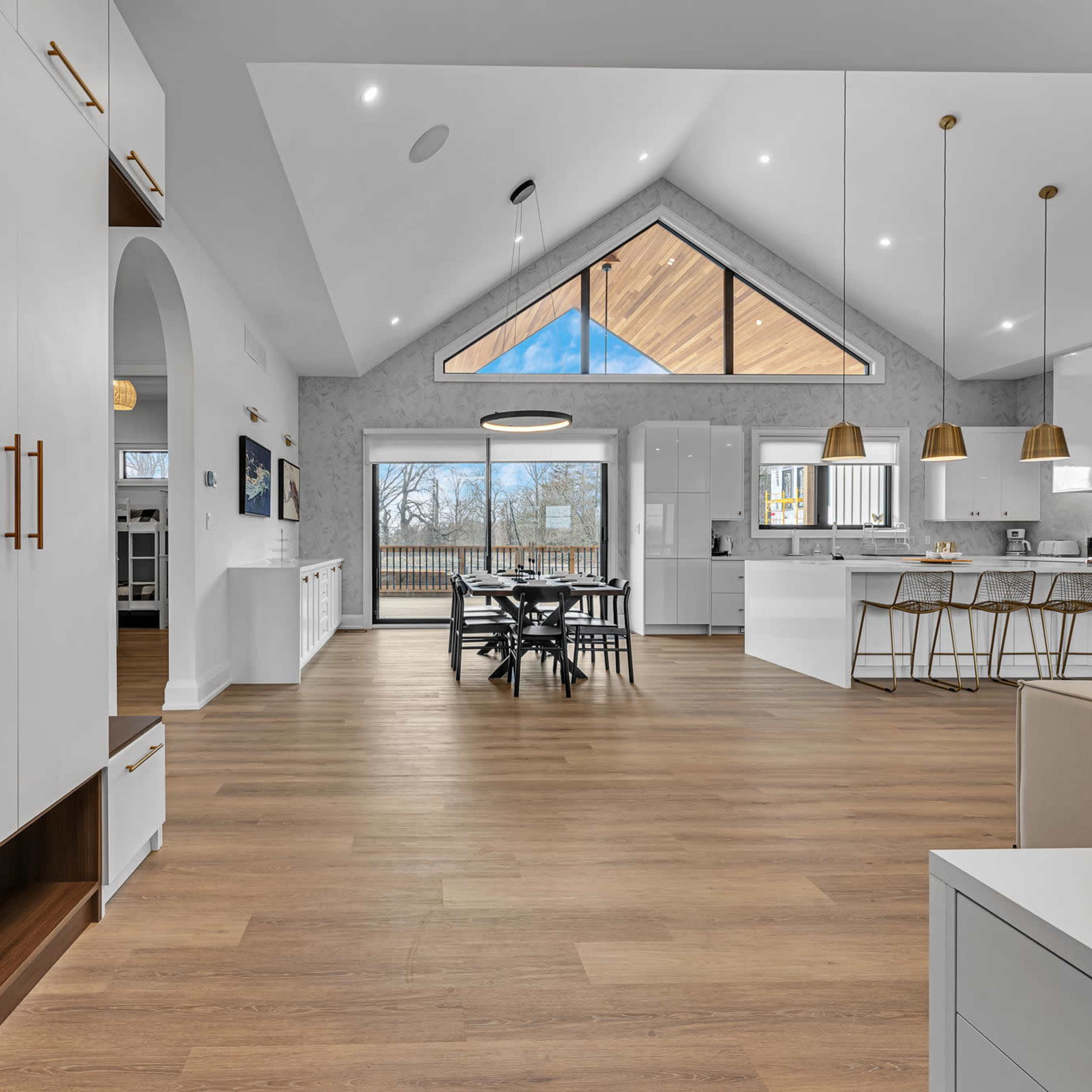 A modern kitchen and dining area with large windows, wooden flooring, and high ceilings featuring a triangular design.