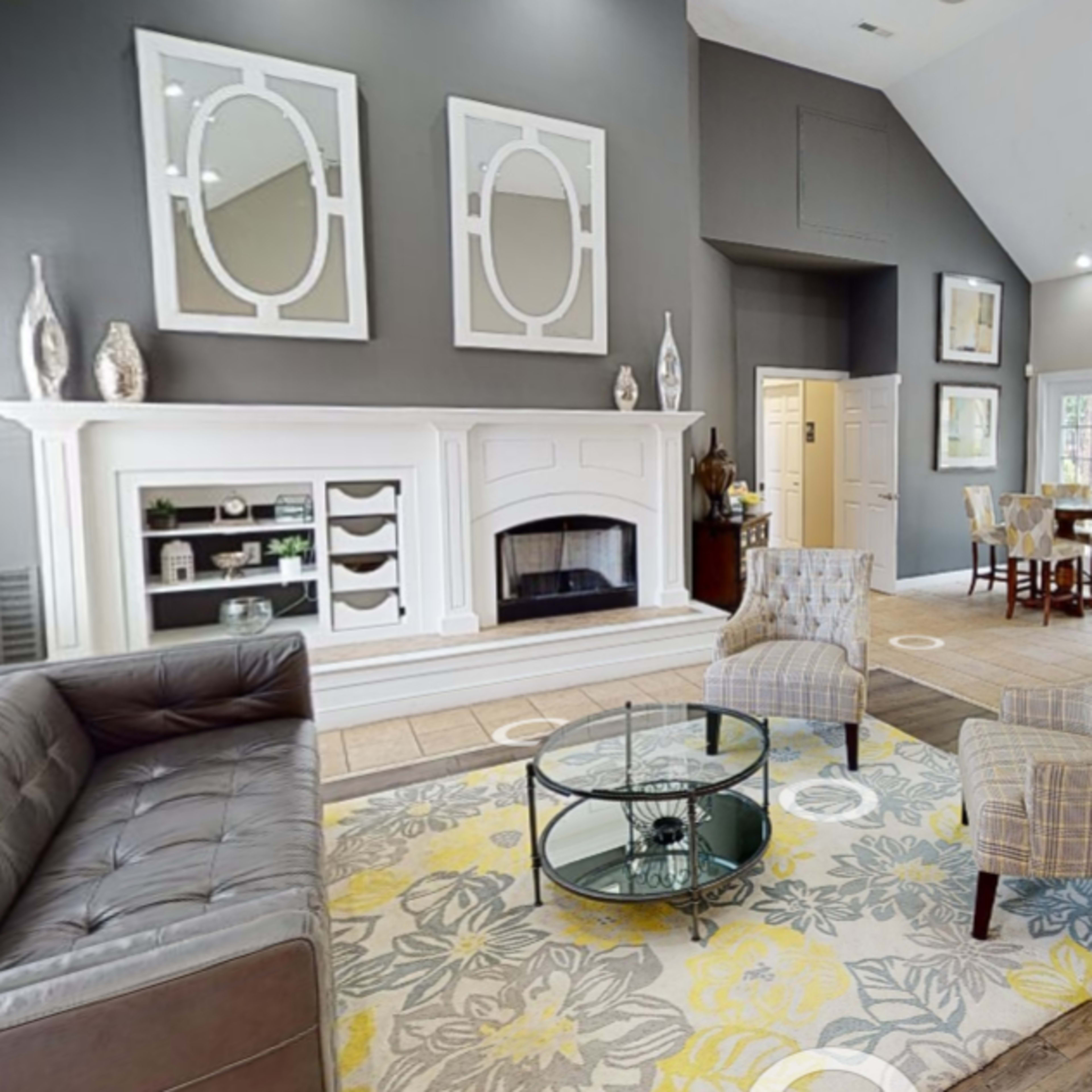 A modern living room features a dark gray accent wall, a fireplace with a white mantel, a patterned area rug, and seating arrangements with a glass coffee table.