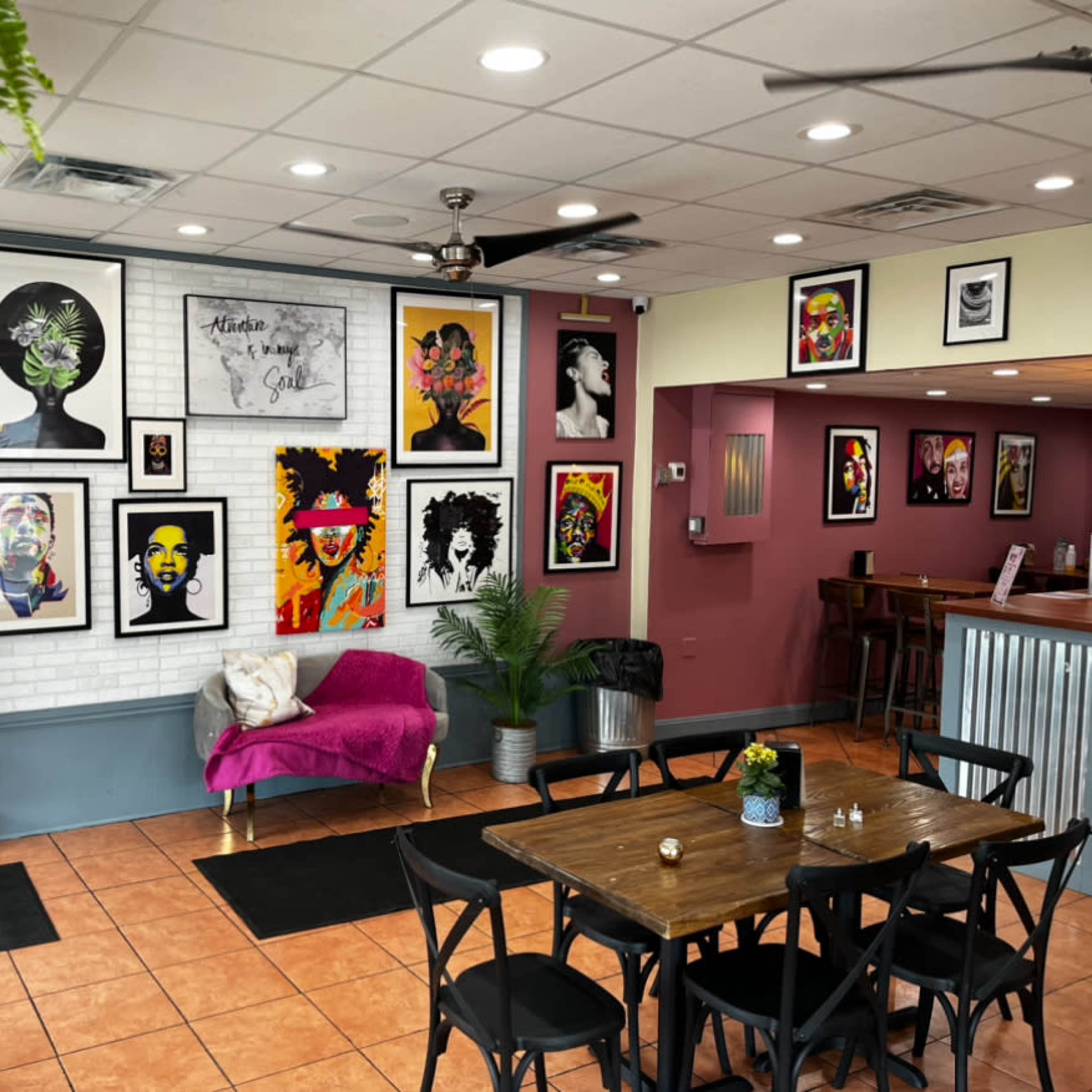 A vibrant cafe interior decorated with colorful portraits on the walls, a pink couch, and wooden tables for seating.