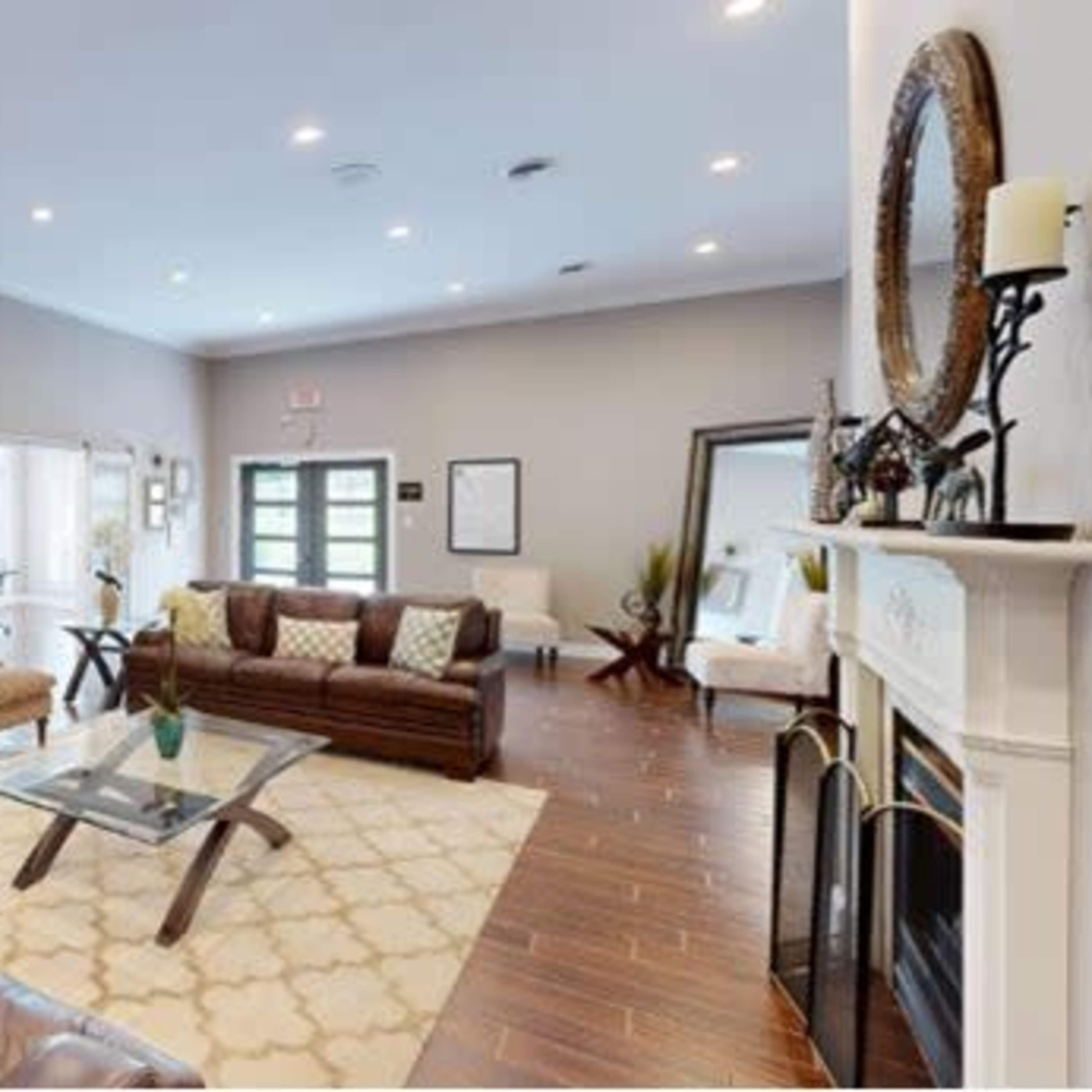 A spacious living room featuring two leather sofas, a glass coffee table, and decorative artwork on the walls, with large windows allowing natural light in.