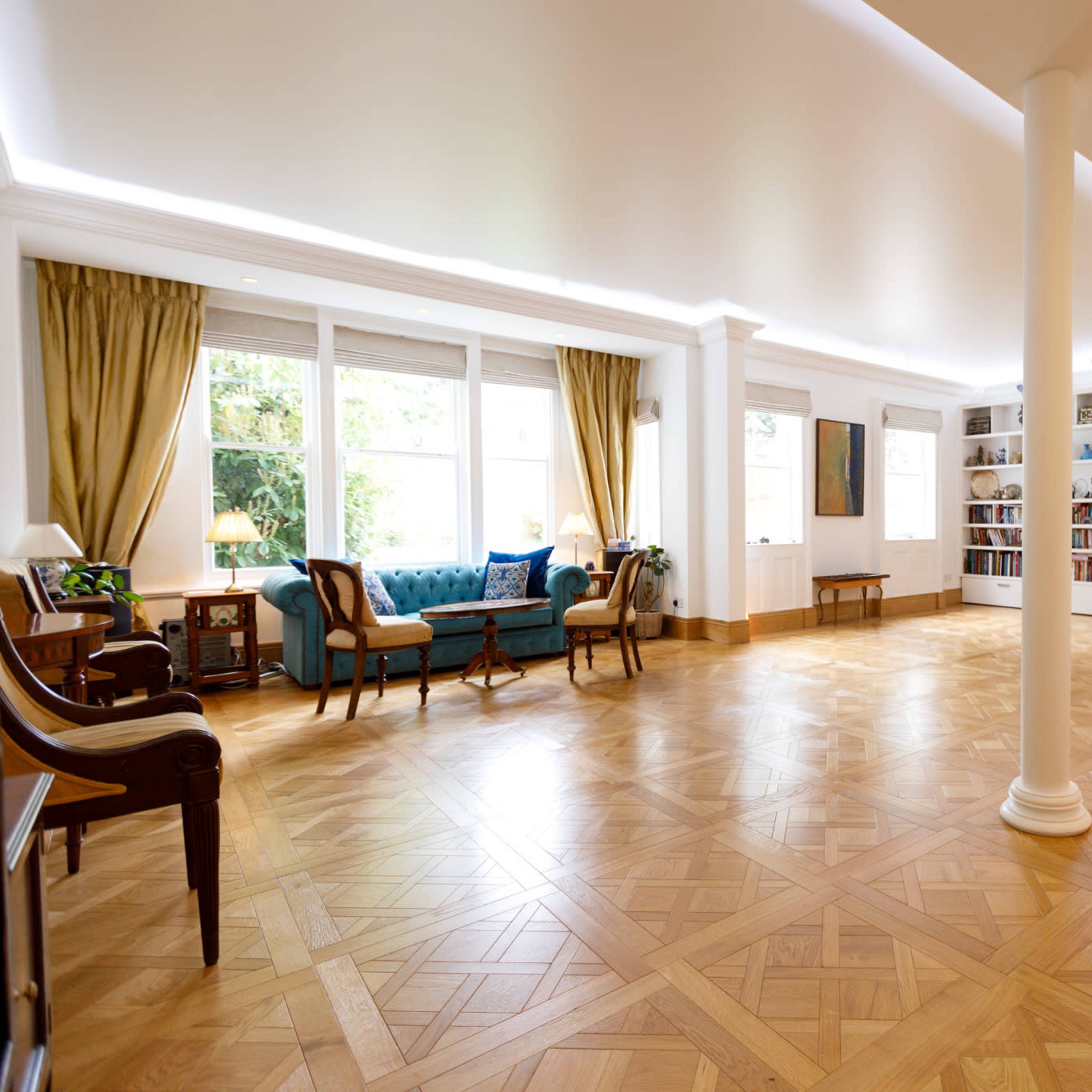 A spacious living room with wooden flooring, large windows, and a mix of modern and traditional furniture.