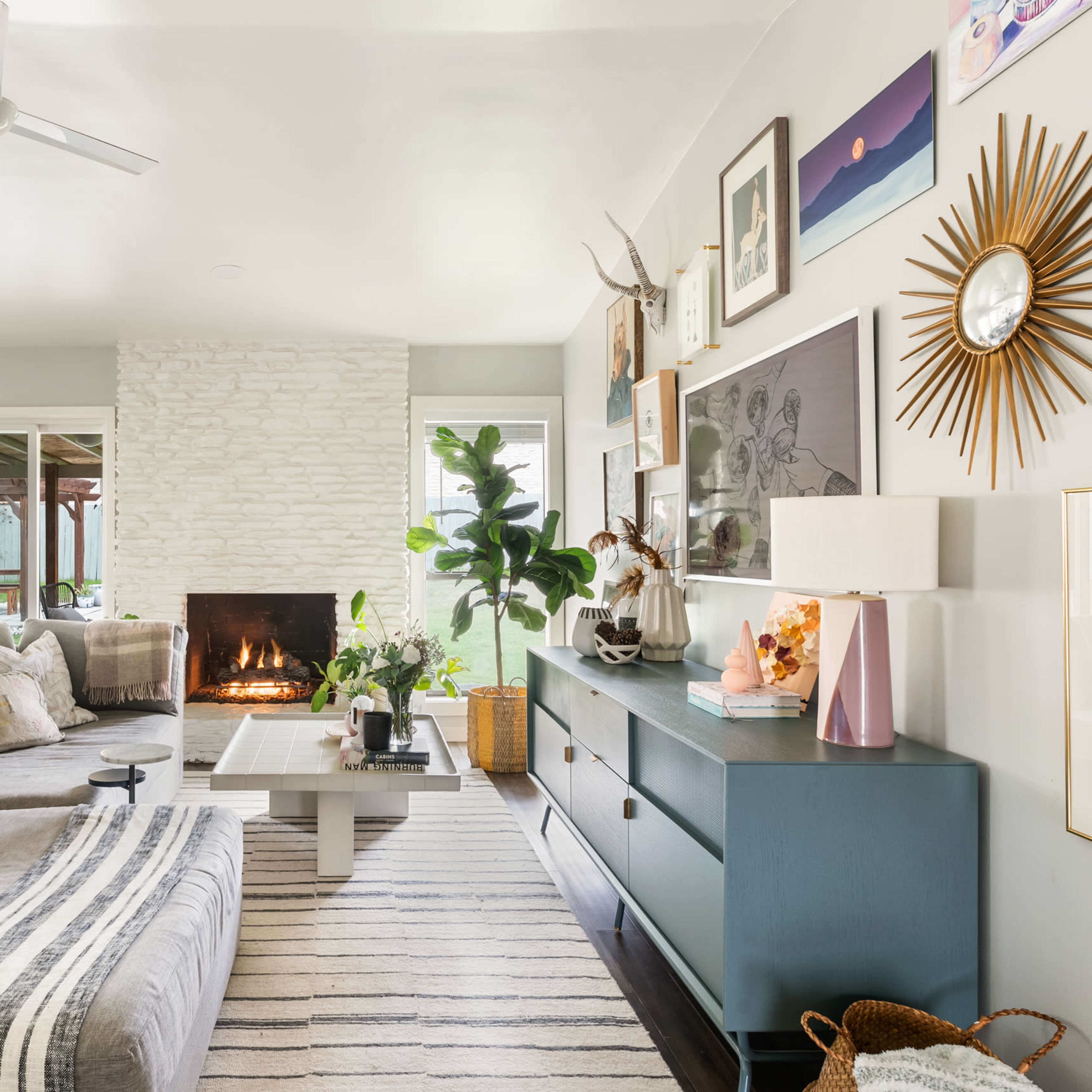 The living room features a sectional couch, a coffee table, a stone fireplace, and large windows that open to an outdoor space.