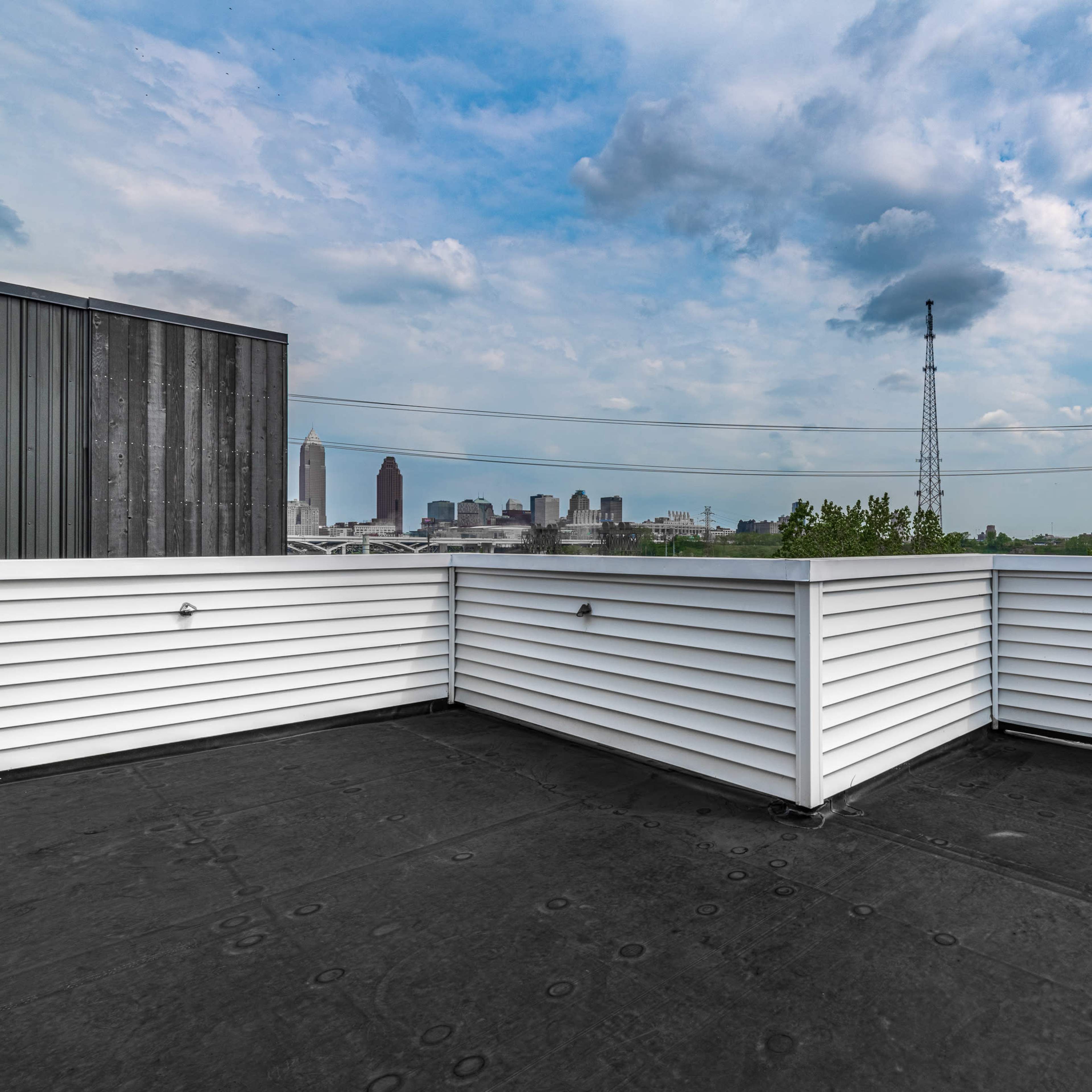 A rooftop terrace with white railings overlooking a city skyline under a partly cloudy sky.
