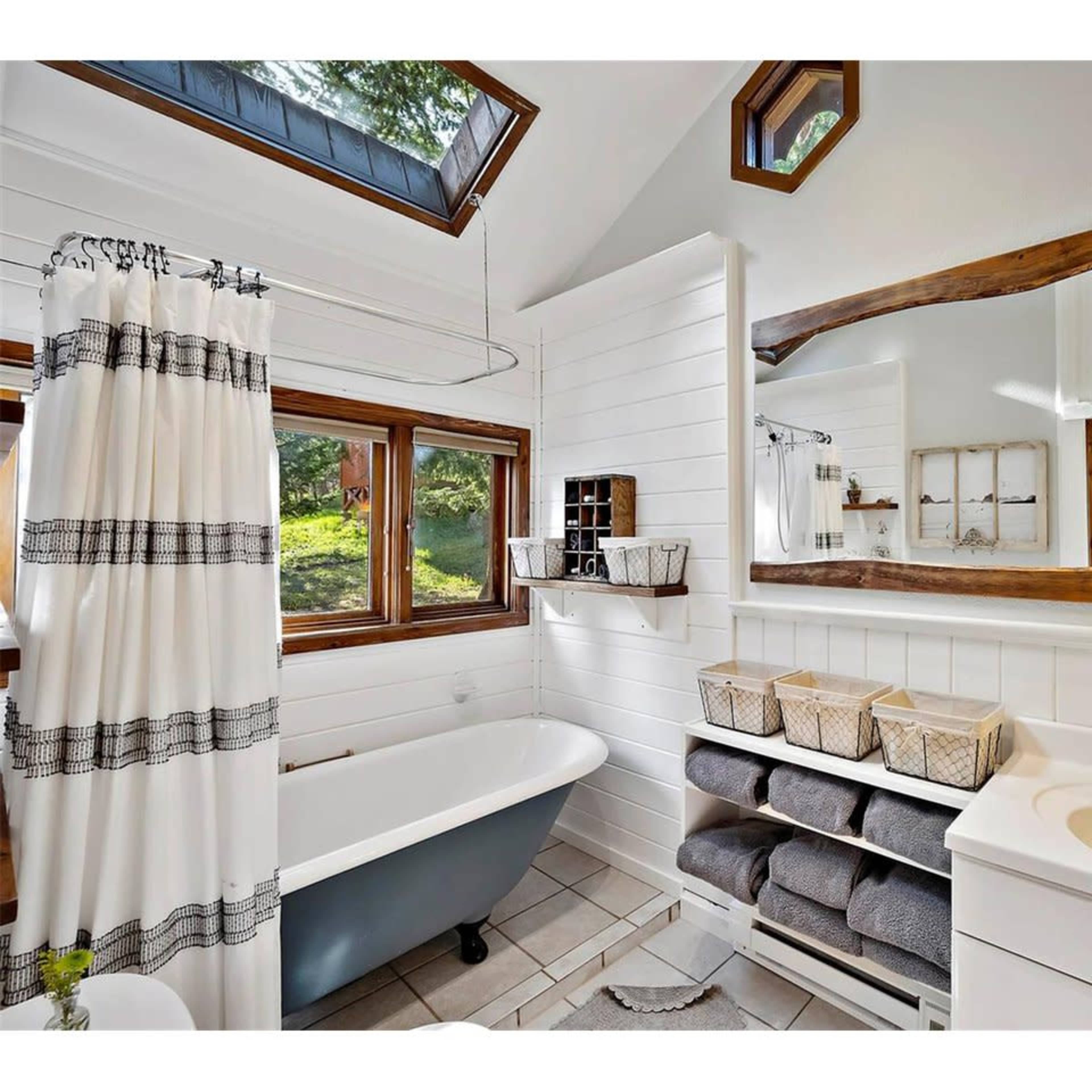 The bathroom features a freestanding bathtub, a sink with a mirror, and shelves filled with neatly stacked towels, all illuminated by natural light from windows.