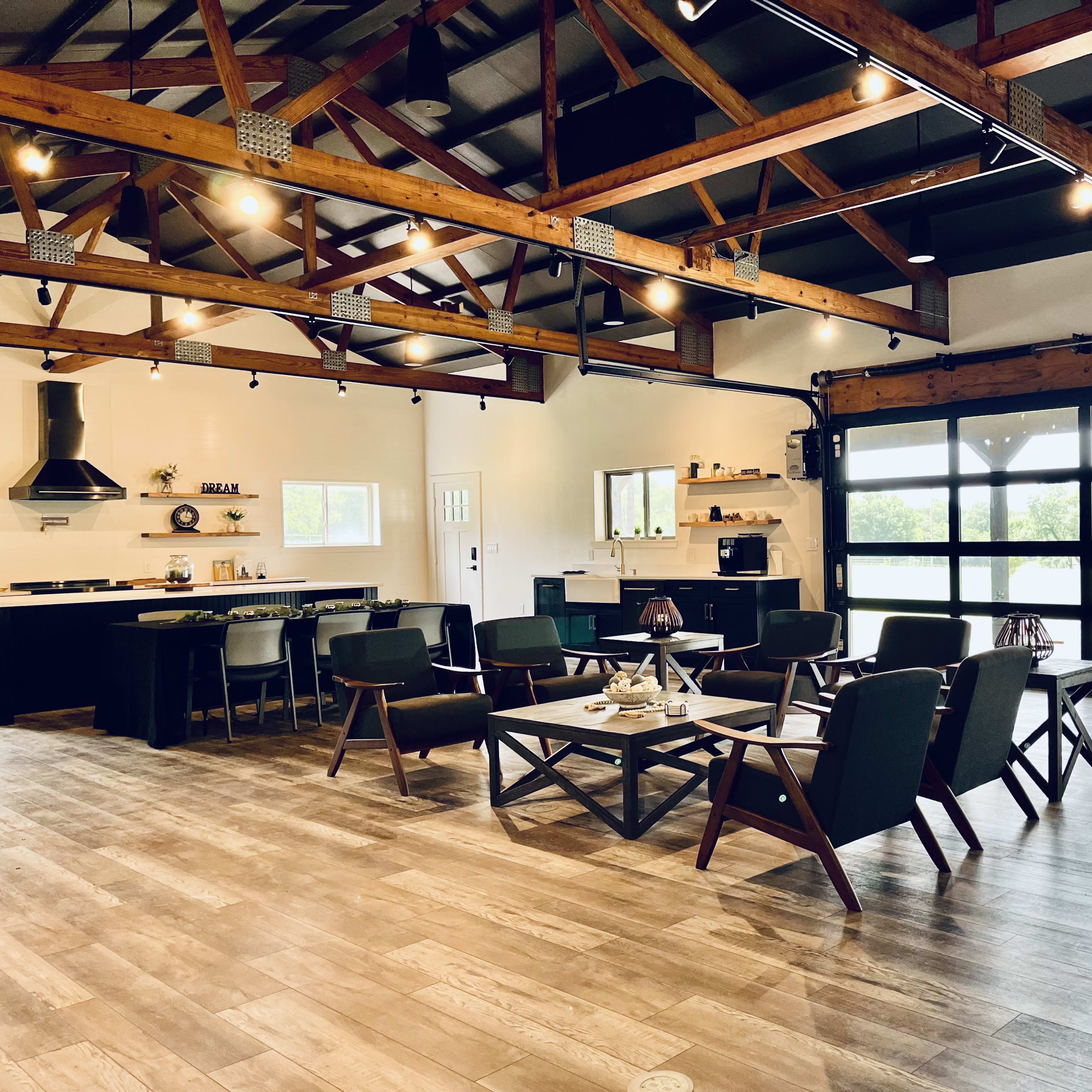 A spacious, modern interior with exposed wooden beams, a kitchen area, and seating arrangements around a central coffee table.