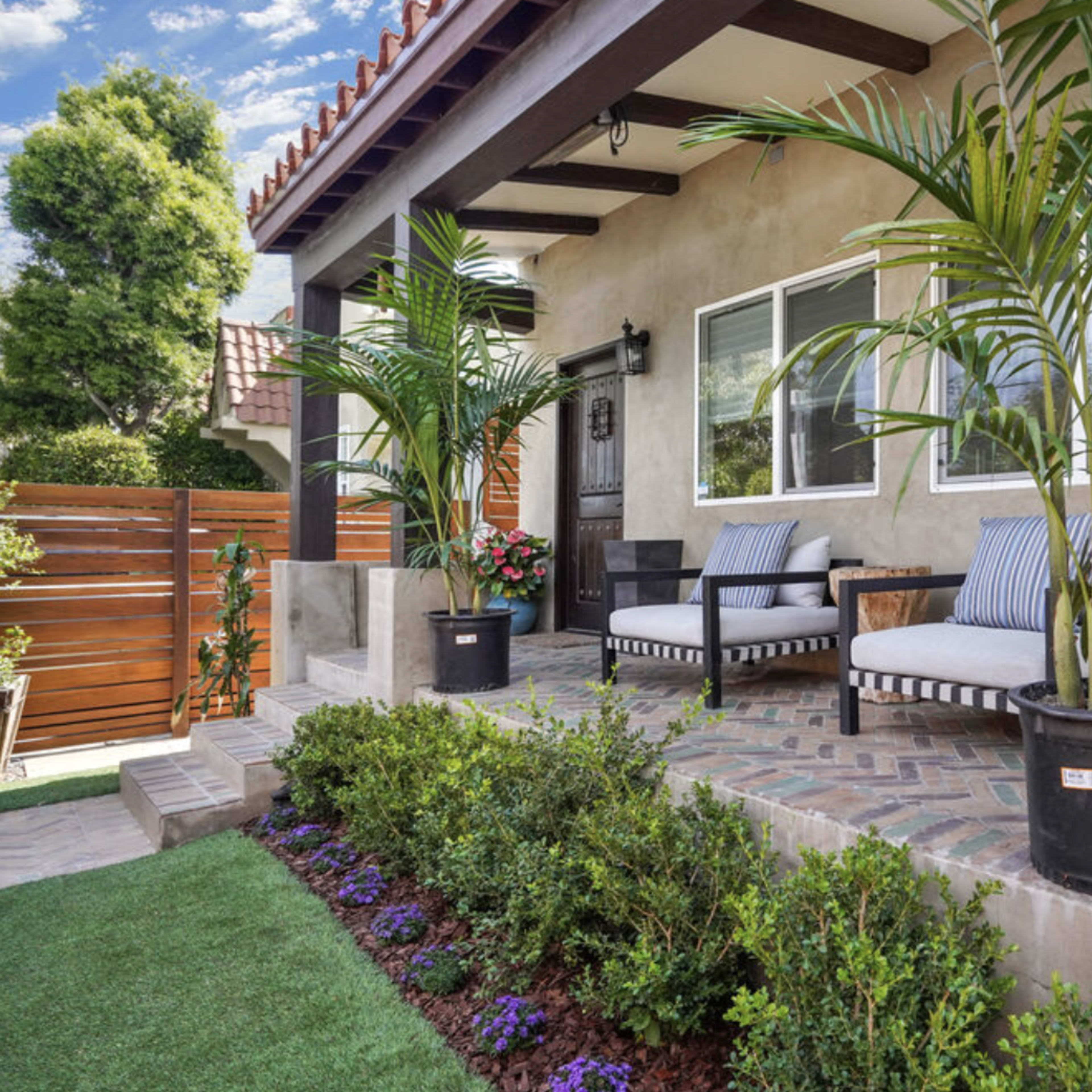 A front porch of a house with two chairs, potted plants, and a landscaped area.