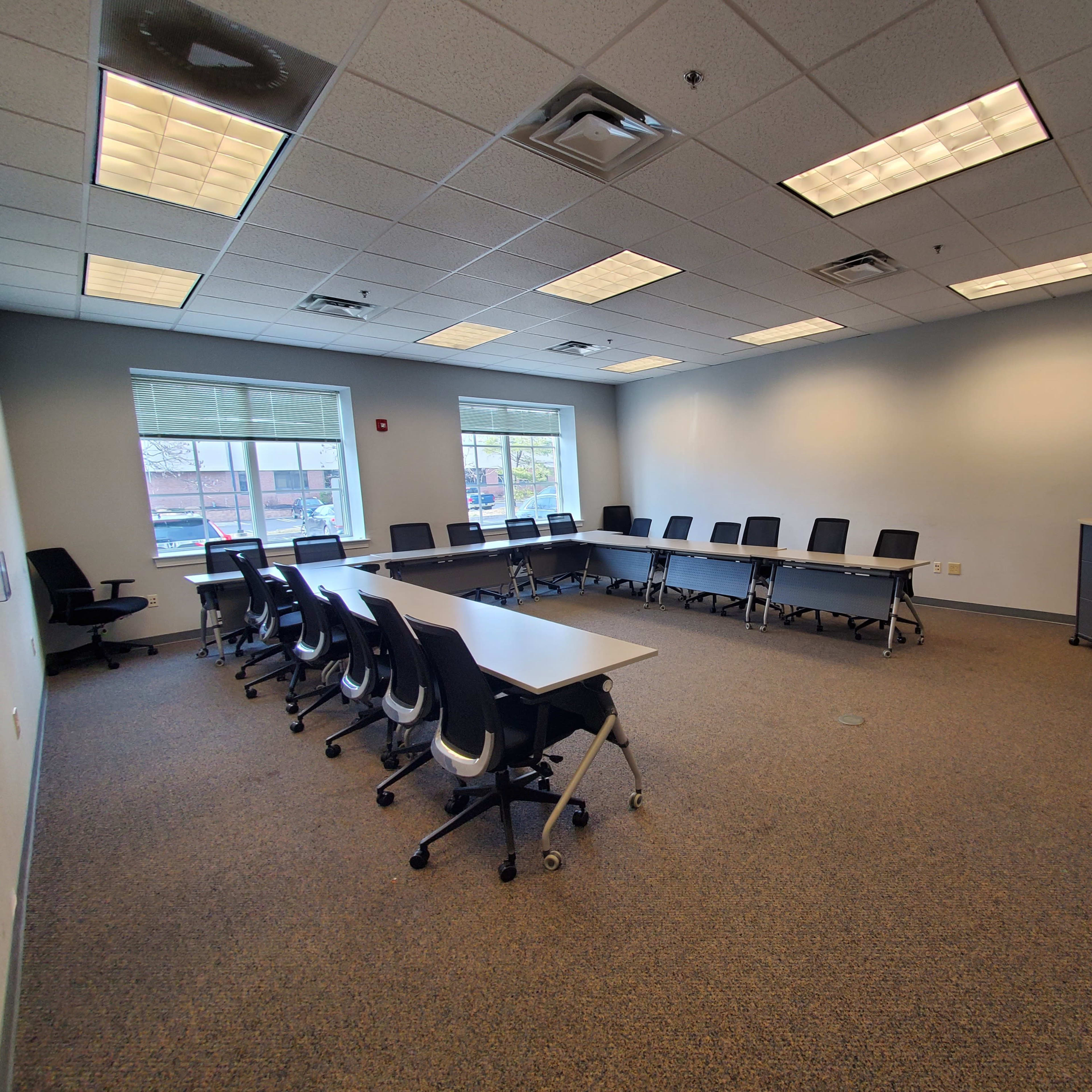 A conference room features a long table surrounded by chairs, with a large screen and an American flag against the wall.