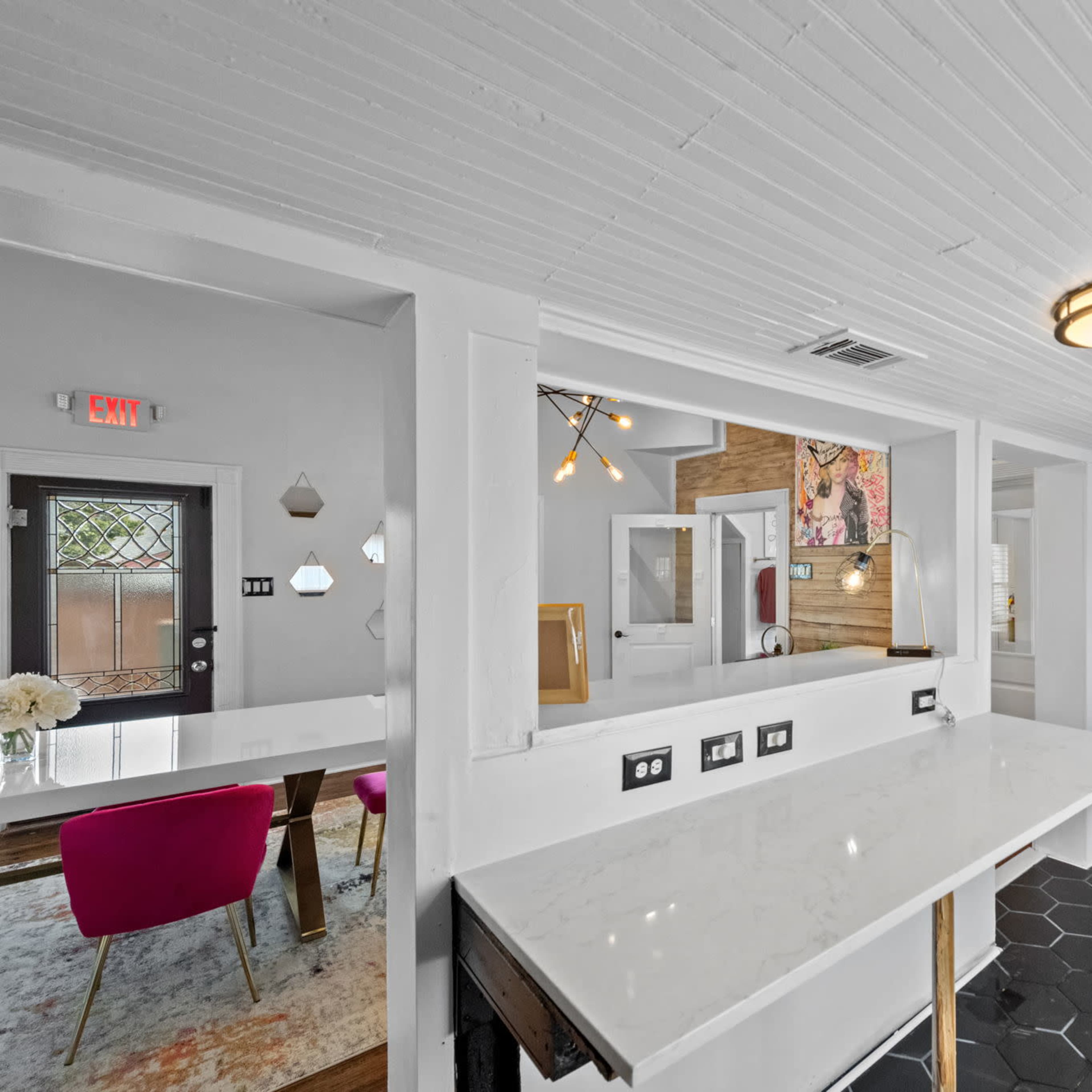 A modern interior space with a white countertop, black cabinetry, and a hexagonal tile floor, seamlessly connecting a dining area to a well-lit room.