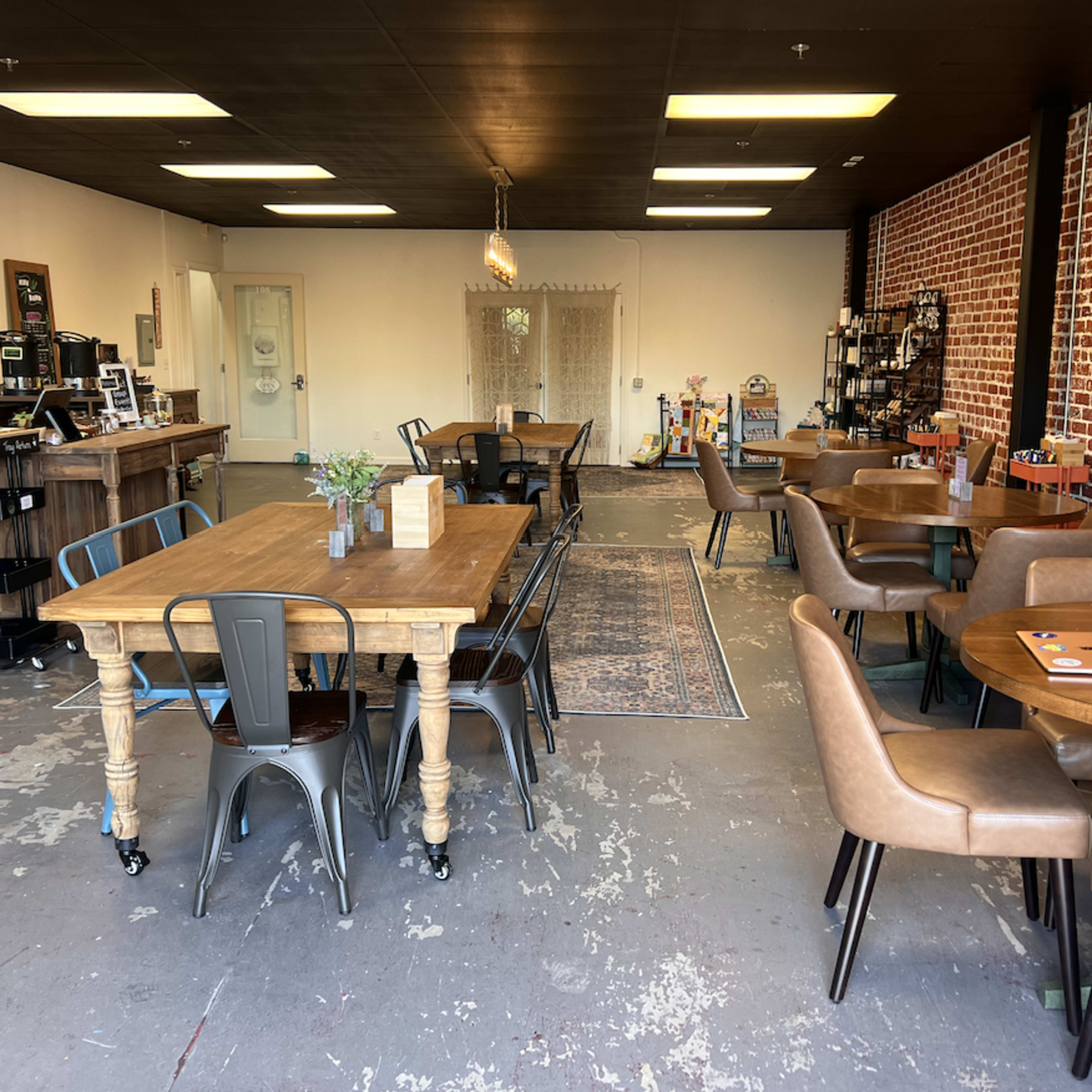 A spacious café interior with wooden tables, metal chairs, and a brick wall.