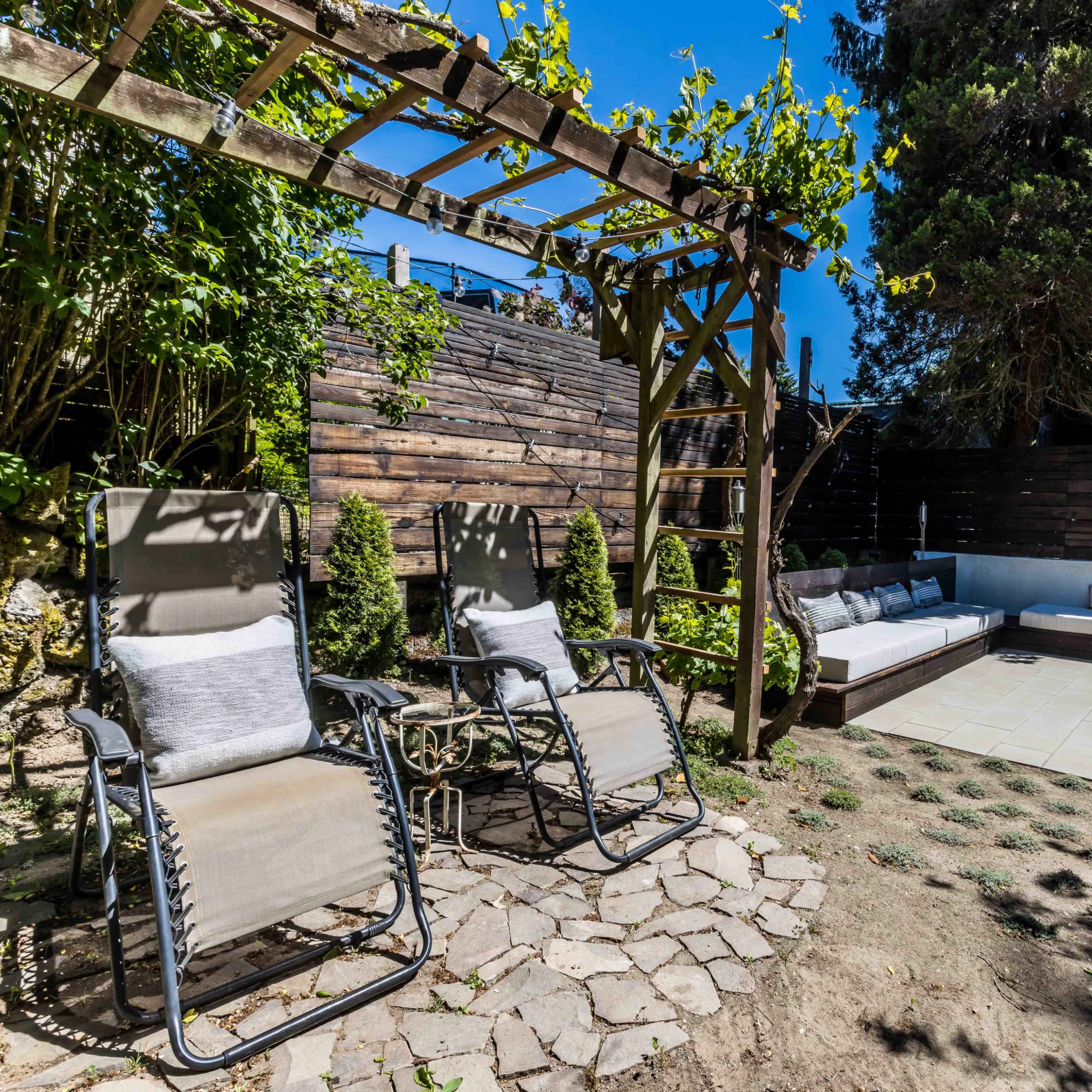 A landscaped garden area with two lounge chairs, a seating arrangement, and a wooden trellis covered with greenery.
