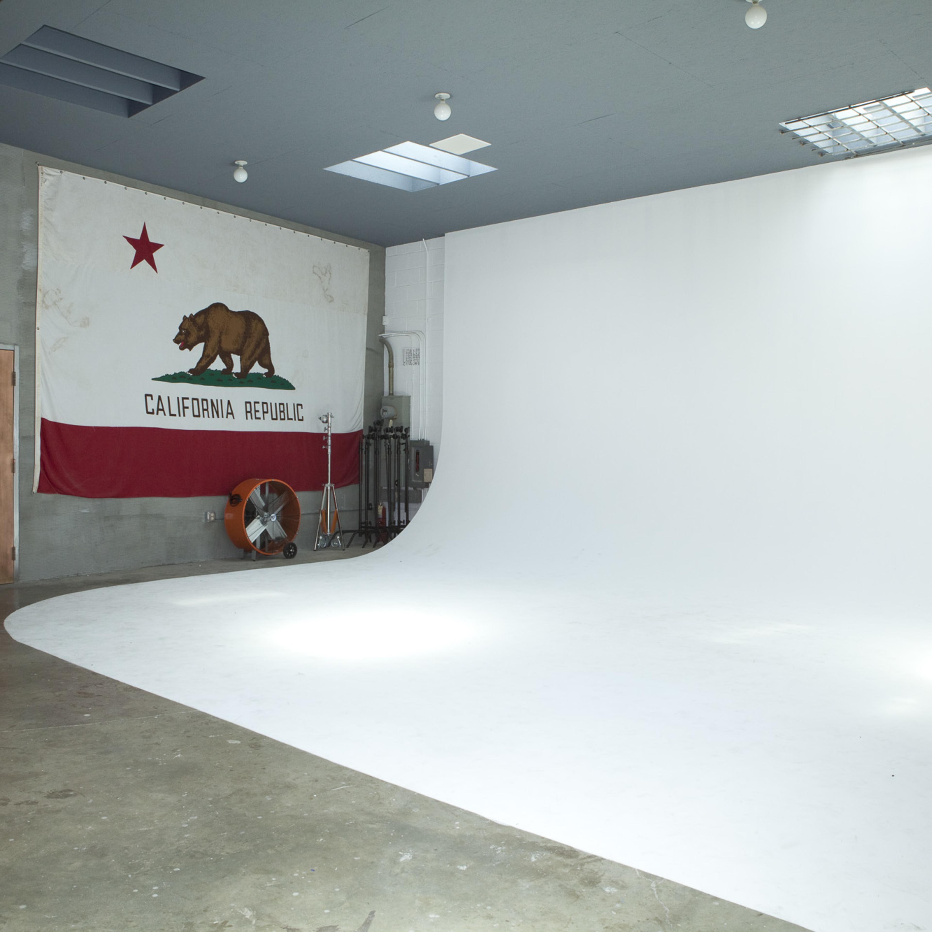A spacious studio with a large white backdrop and a California state flag hanging on the wall.