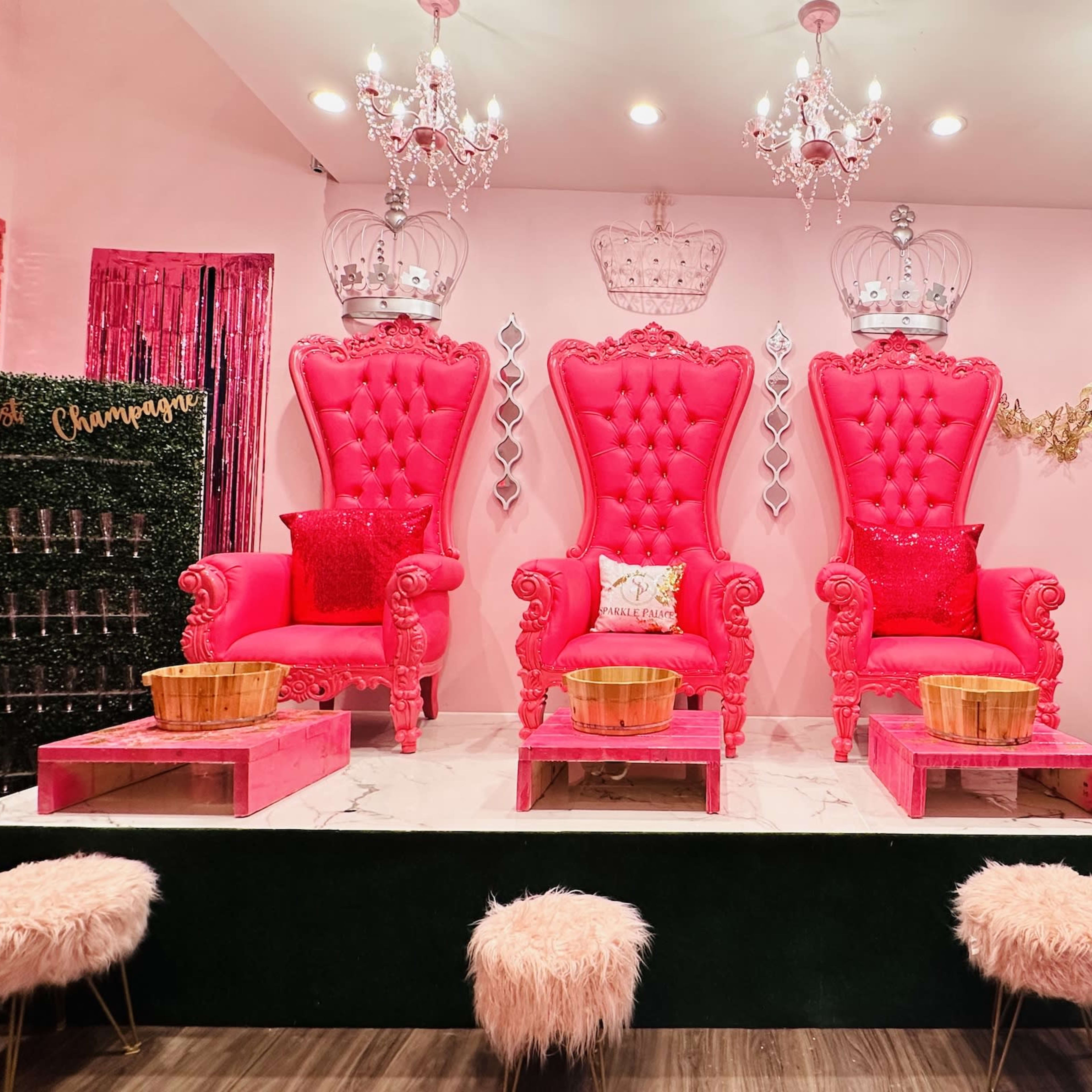 A vibrant pink room featuring three ornate, high-backed chairs with crowns, surrounded by decorative elements like chandeliers and plush seating.