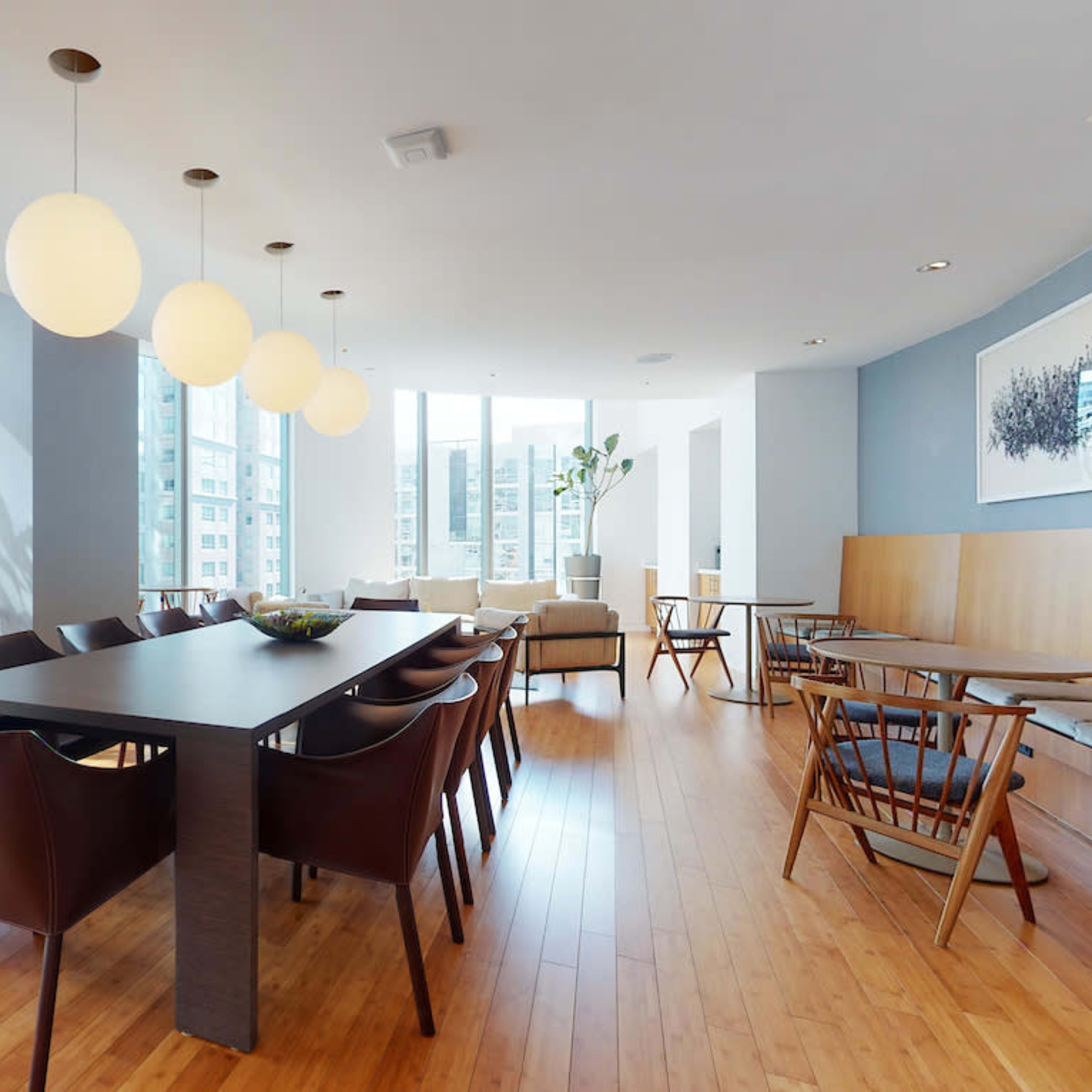 A modern dining area with large windows, a long table surrounded by chairs, and pendant lighting overhead.