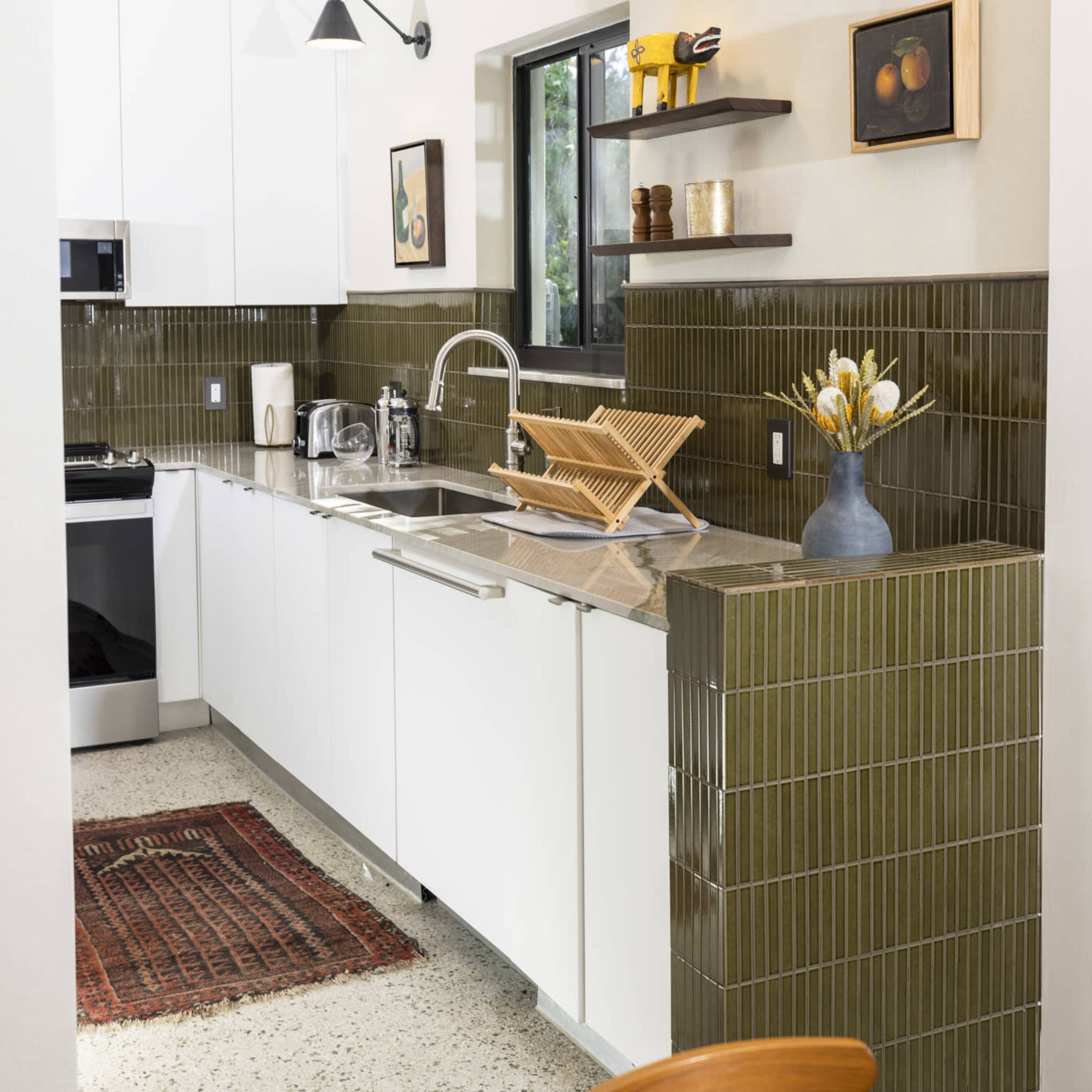 A modern kitchen features white cabinetry, an olive green tiled backsplash, and a marble countertop with stainless steel appliances.