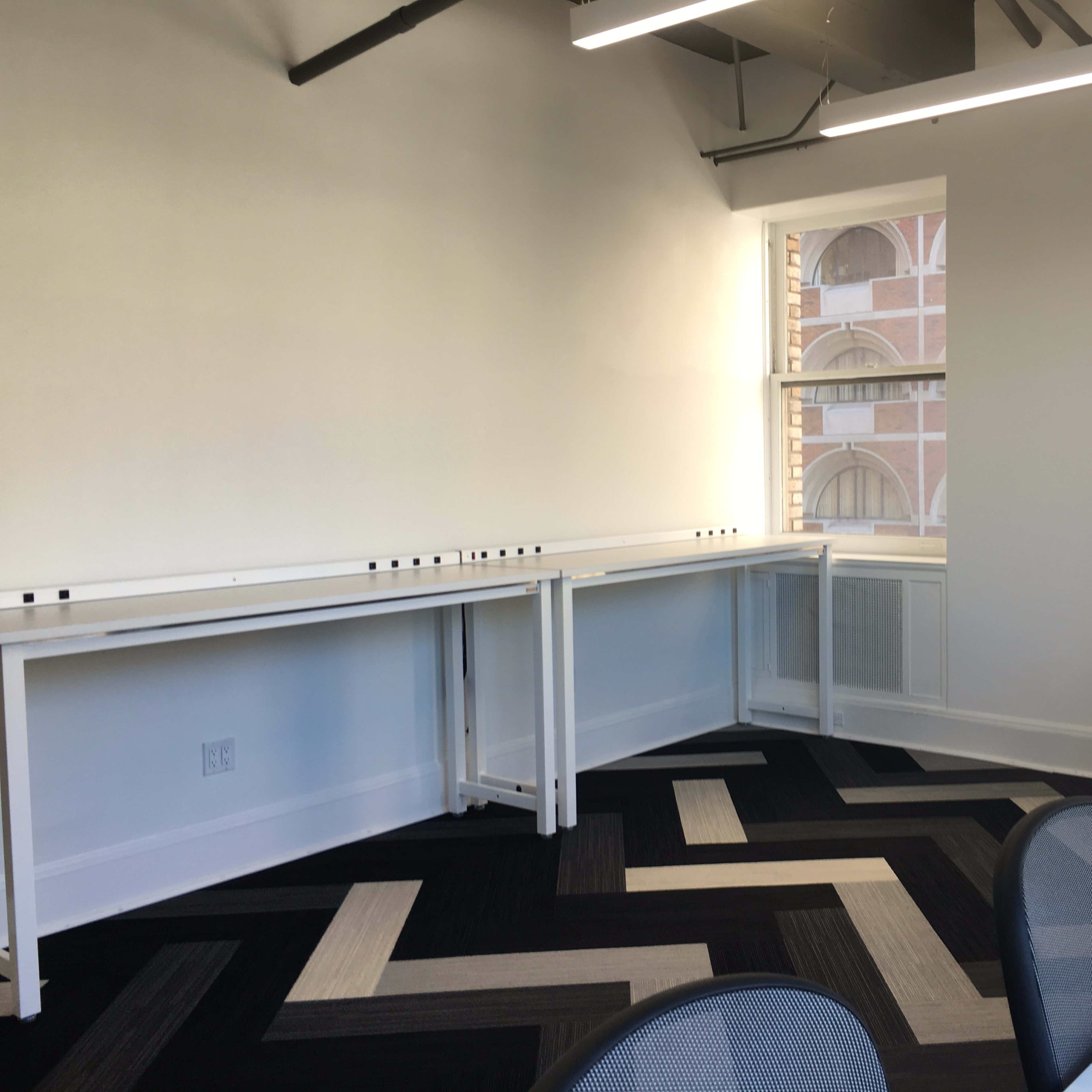 A bright meeting room with two white desks along the walls and a zigzag patterned black and white carpet.