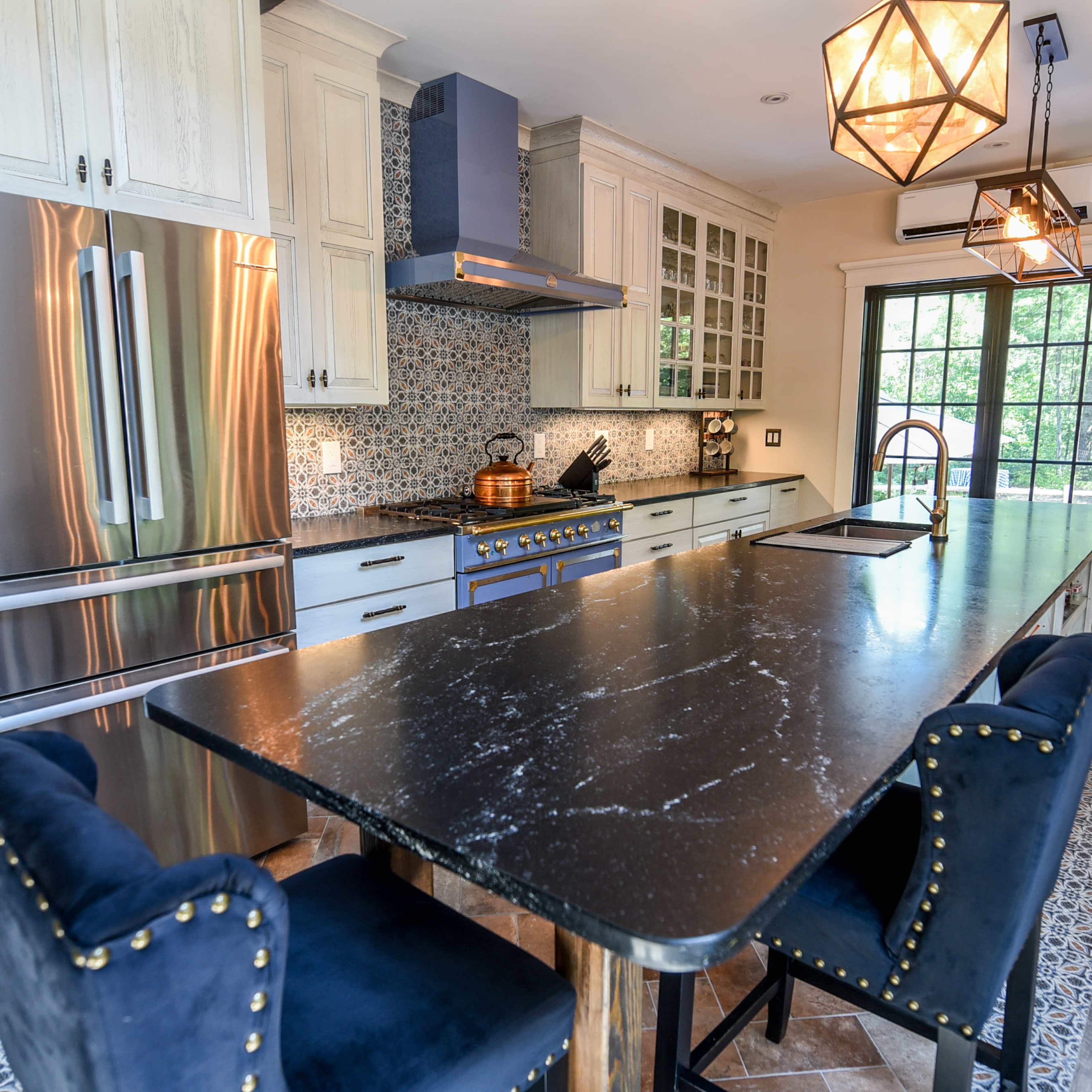A modern kitchen features a large island with dark countertops, stainless steel appliances, and cabinetry with white and blue accents.
